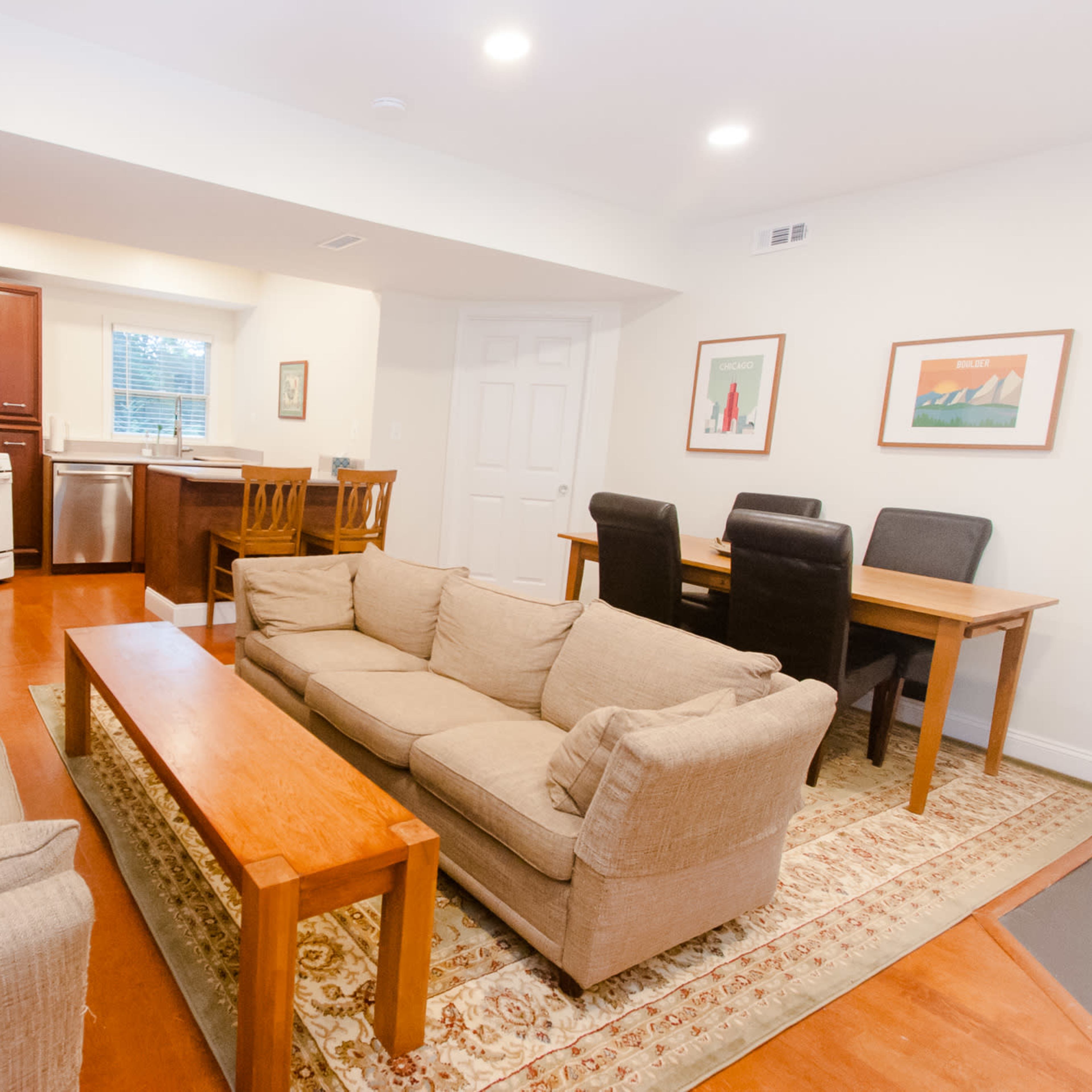 A living space featuring a seating area with two couches, a wooden coffee table, a dining table with chairs, and a kitchenette with appliances.