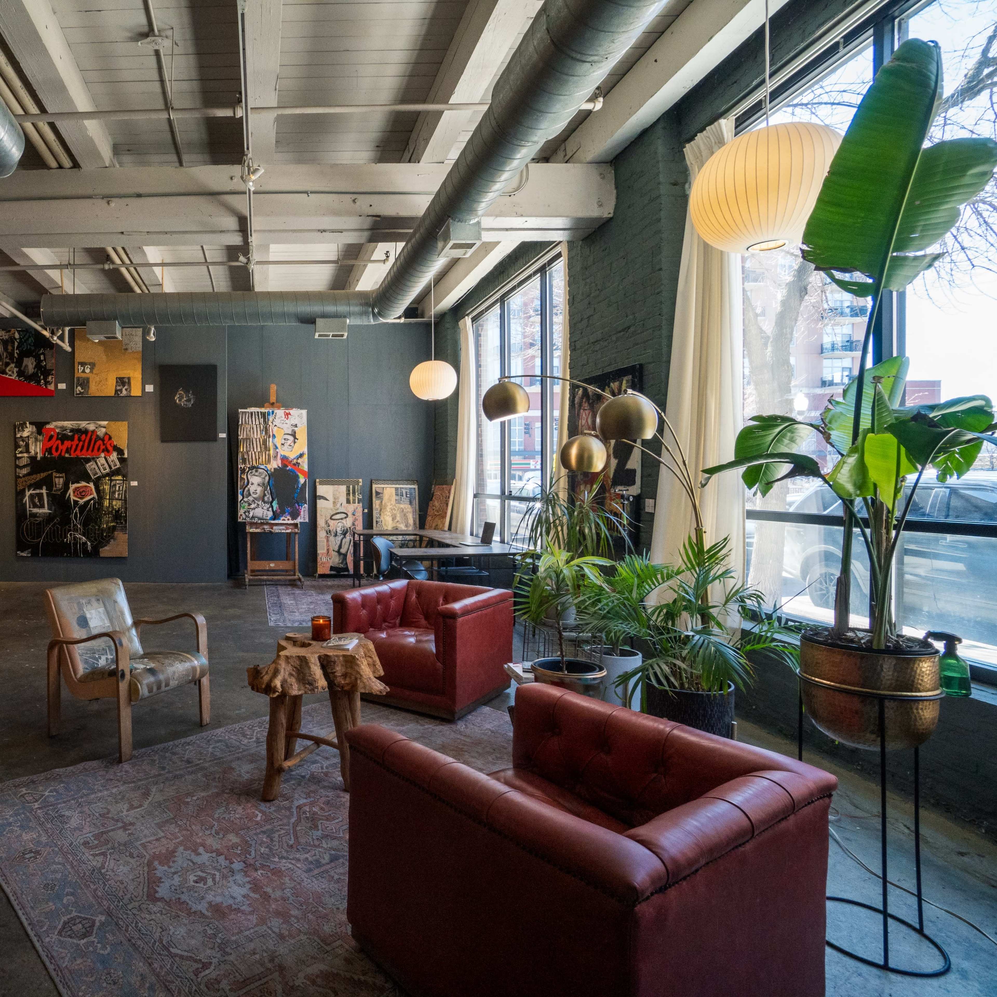 A spacious, artistic interior with red leather sofas, a wooden chair, and walls adorned with various pieces of artwork.
