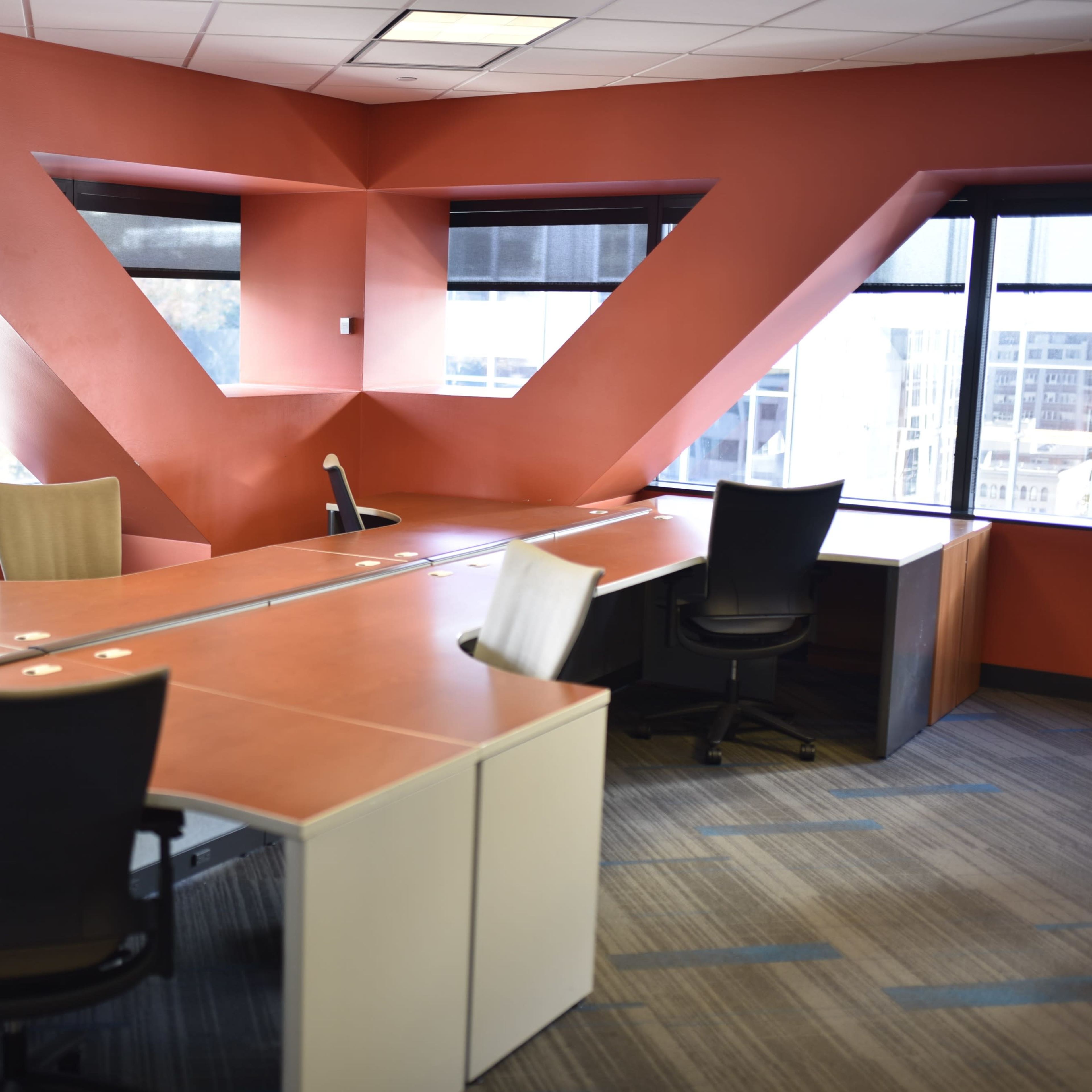 A modern office space with a red accent wall and multiple desks arranged near large windows.