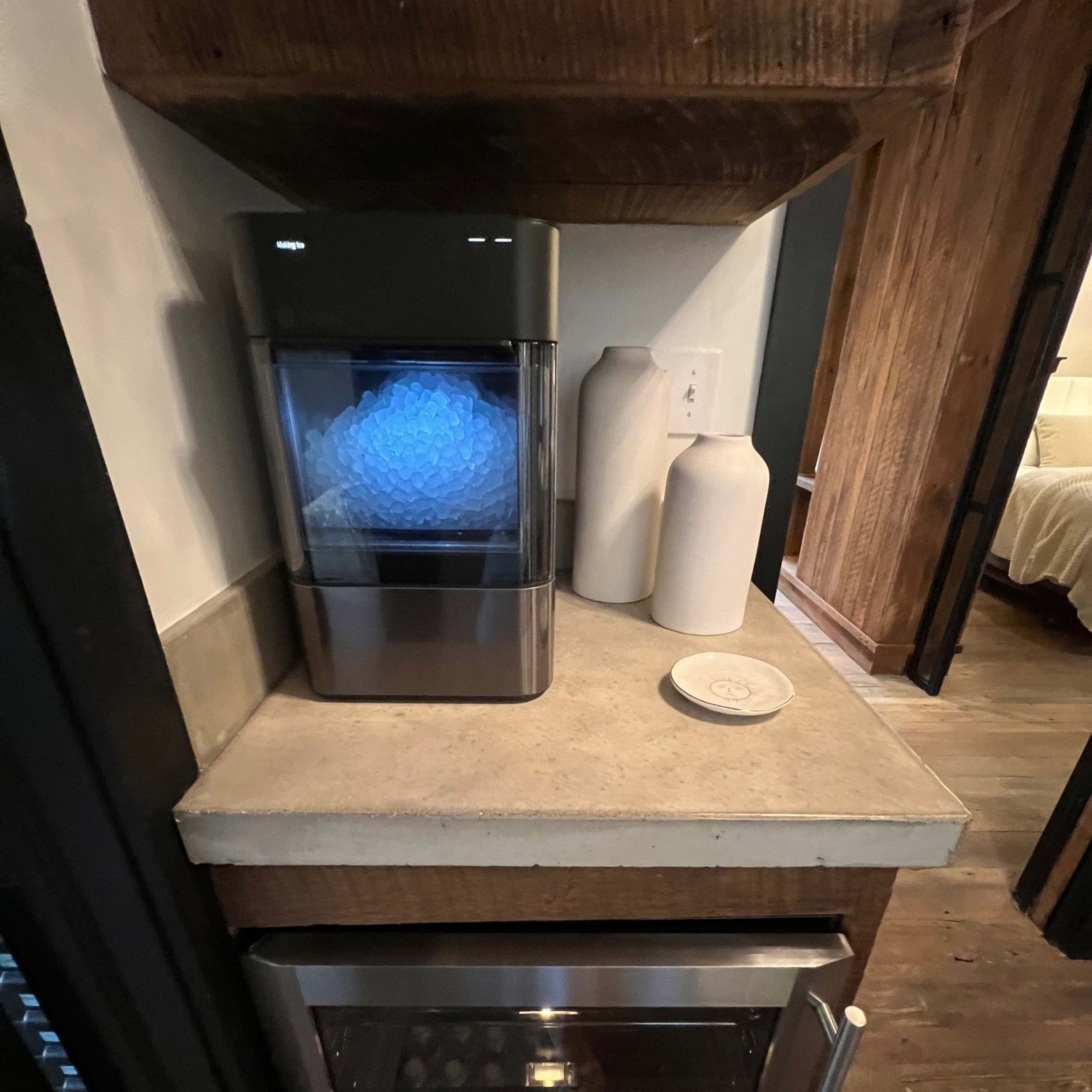 A countertop with an ice maker, two white ceramic containers, and a flat dish, positioned above an under-counter oven in a kitchen setting.