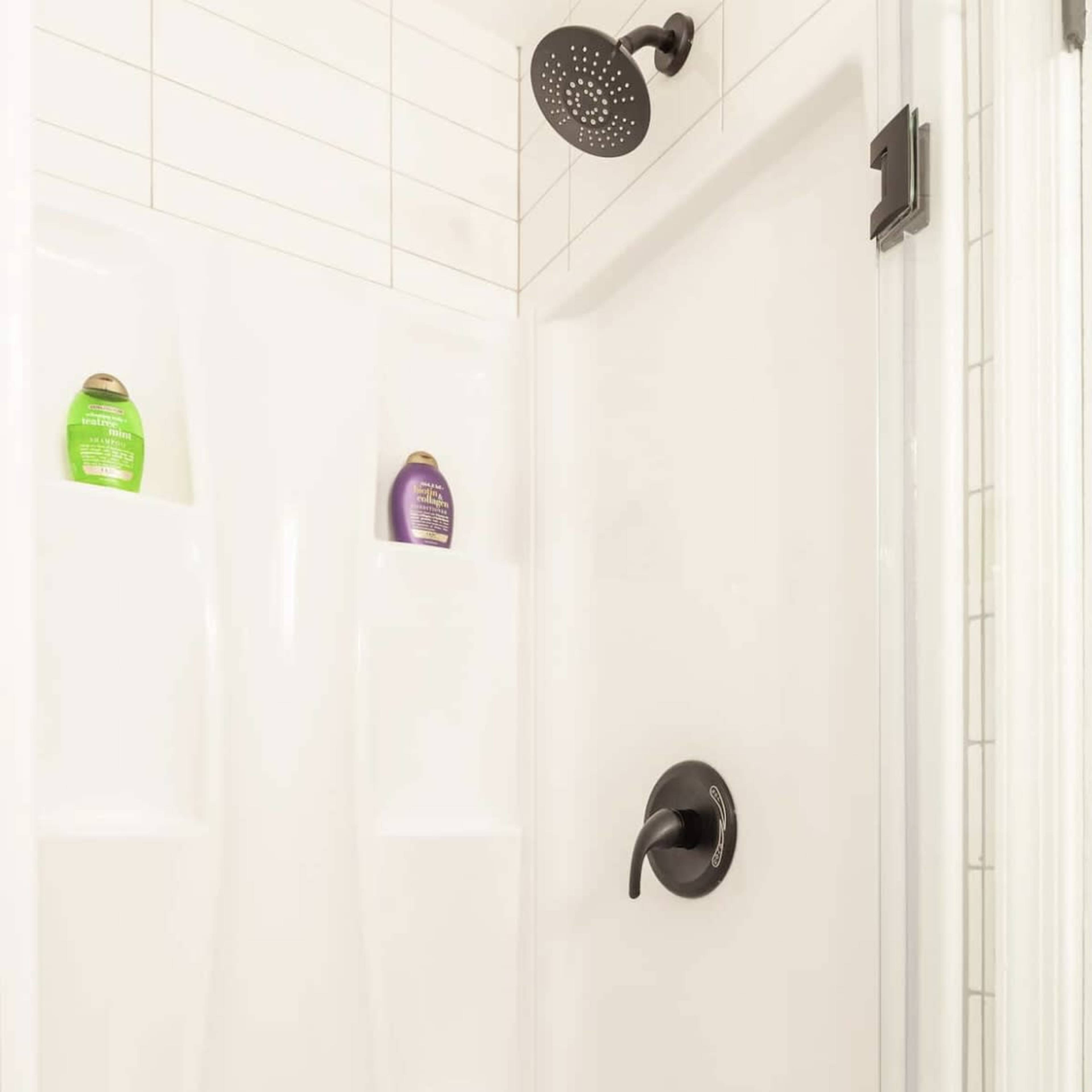 A clean, modern shower stall with a handheld showerhead, a black faucet control, and two shelves containing bottles.