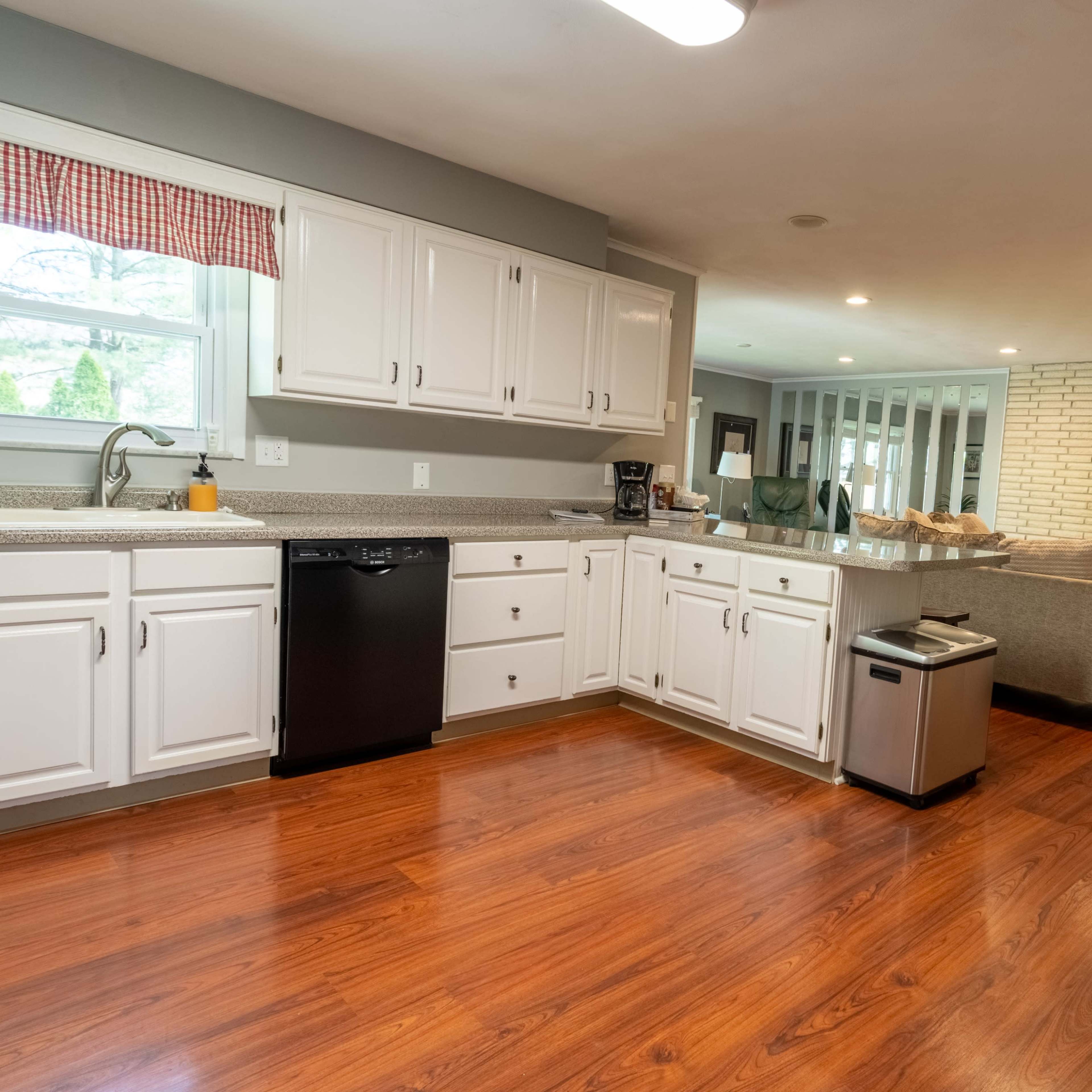 A spacious open-concept kitchen with white cabinets, a granite countertop, and a view into a living area with a fireplace and television.