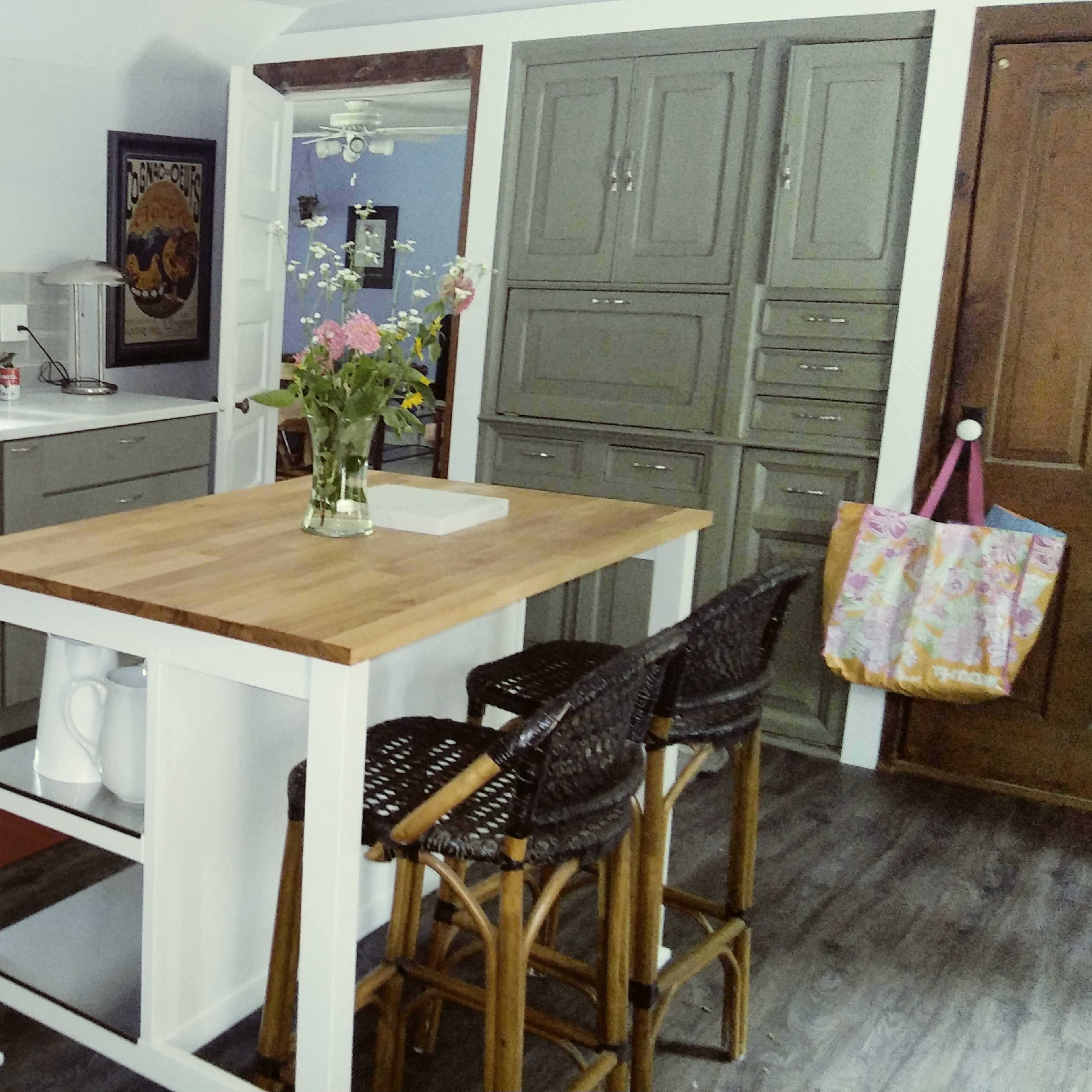 A kitchen with gray cabinets, a stainless steel sink, a wooden island with bar stools, and a vase of flowers on the counter.