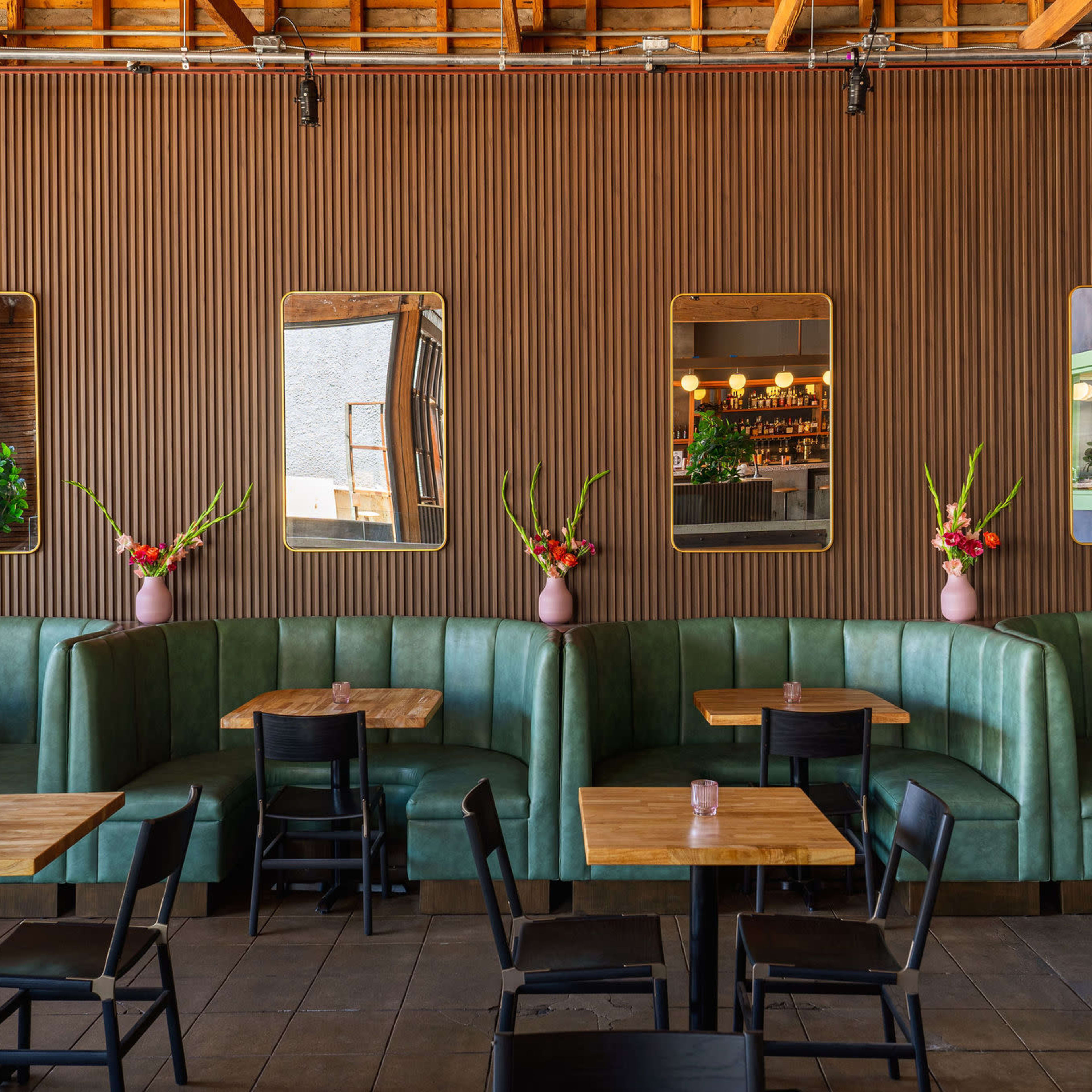 A restaurant interior featuring green seating booths, wooden tables, and large mirrors set in a textured wooden wall.