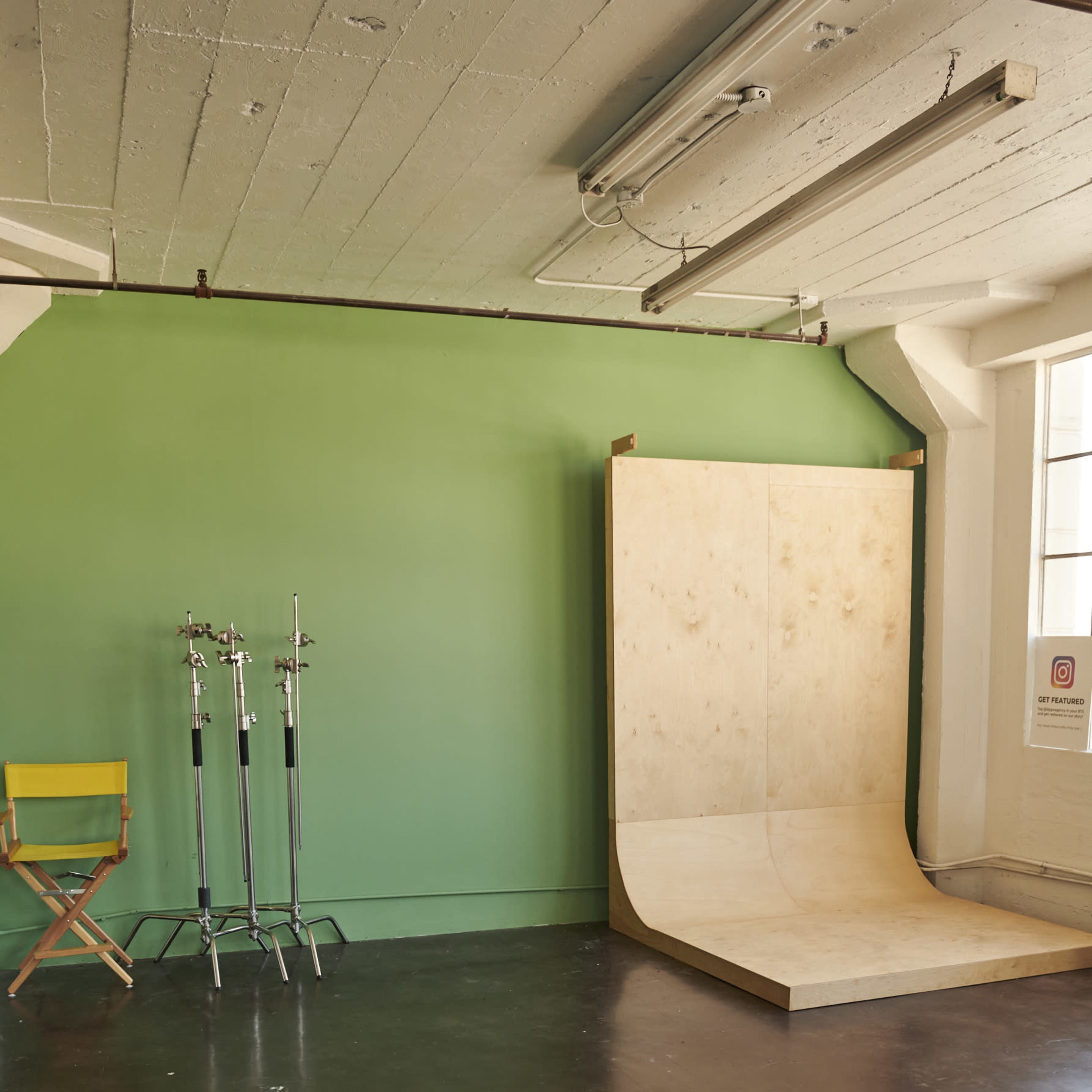 A spacious photography studio with a green backdrop, a ramp structure, and a director's chair next to several light stands.