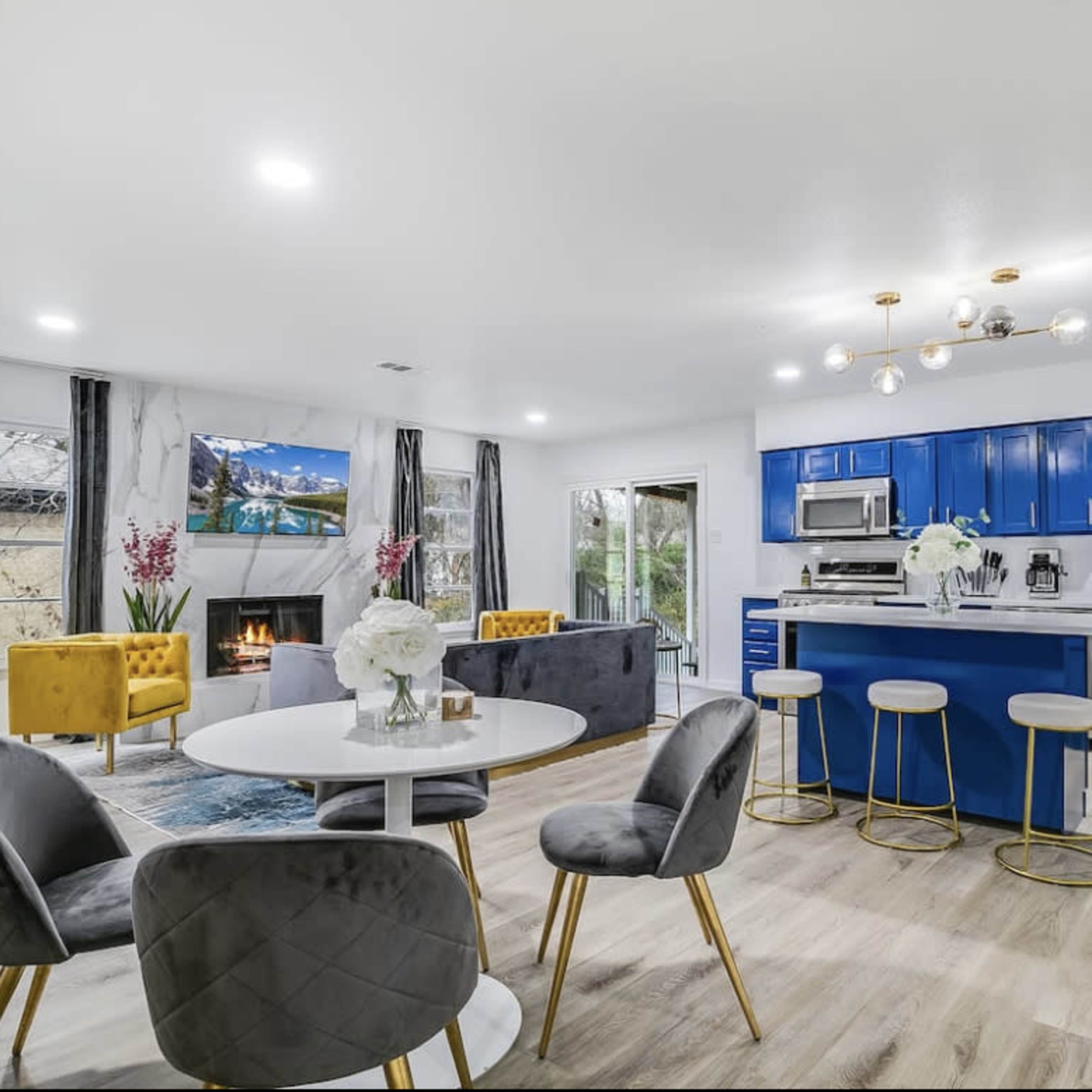 A modern open-concept living space with blue cabinetry, a circular dining table, and a cozy fireplace.
