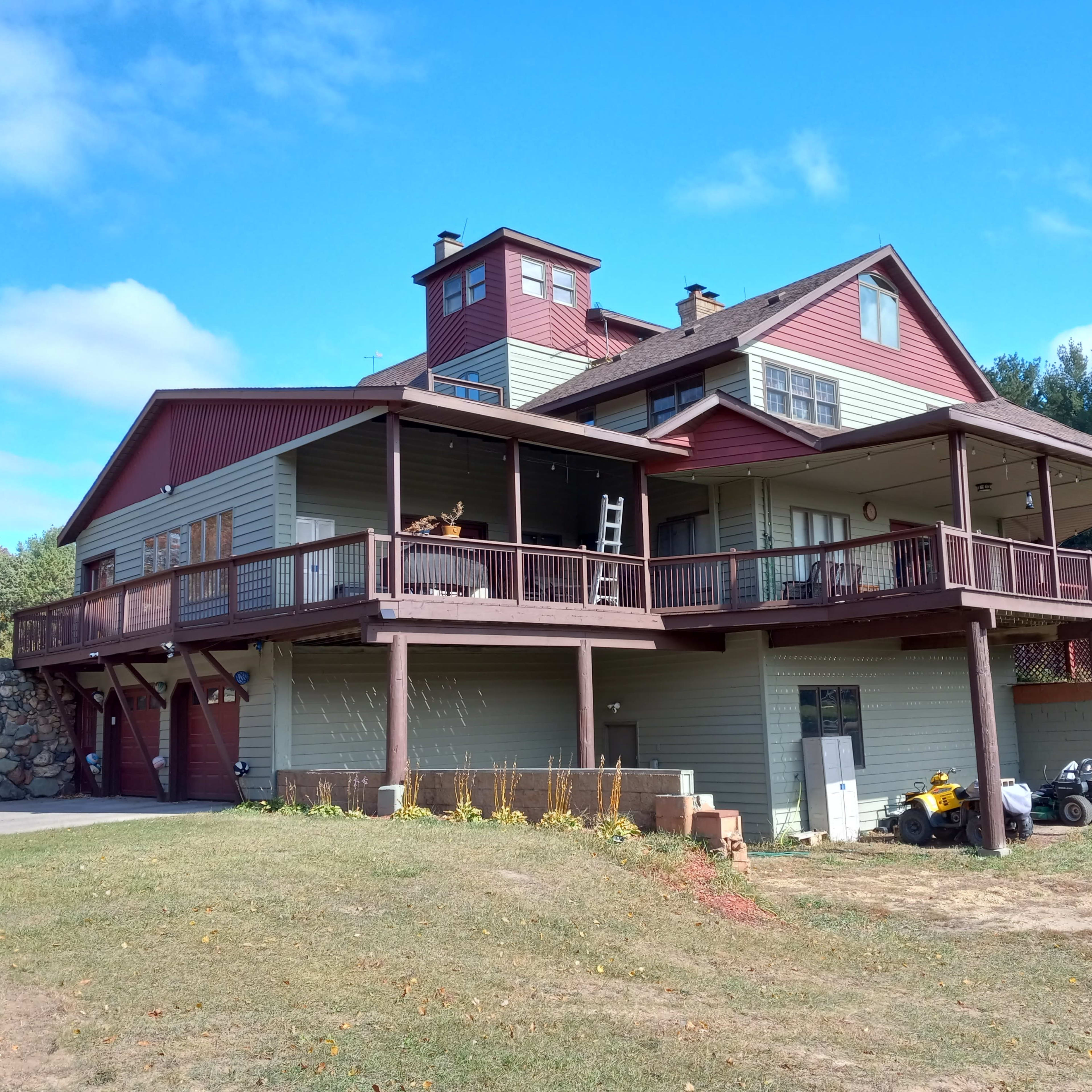 A large, multi-level house with a wraparound porch and a stone wall in the front yard.