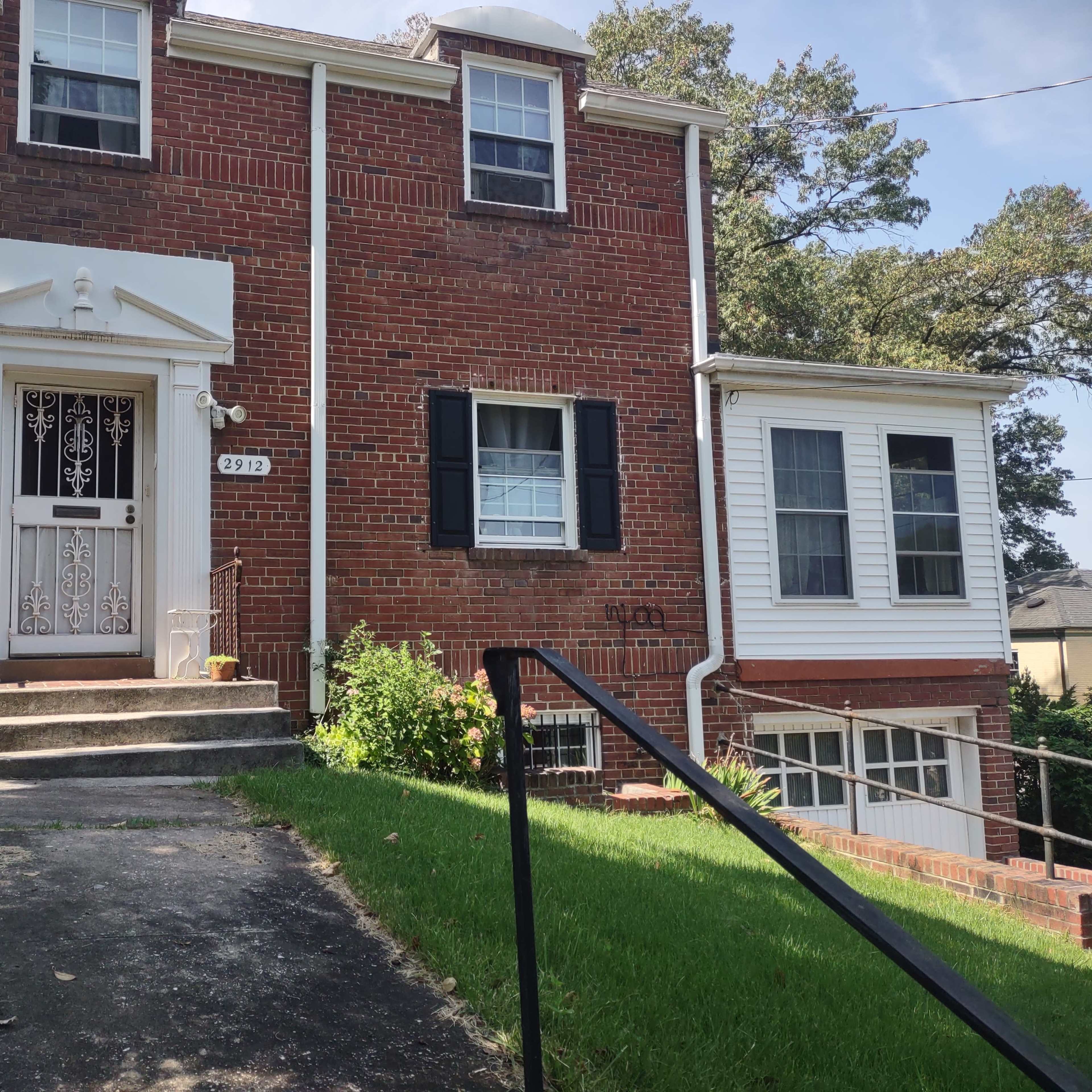 A two-story brick house with white trim, a front porch, and a pathway leading to the entrance.