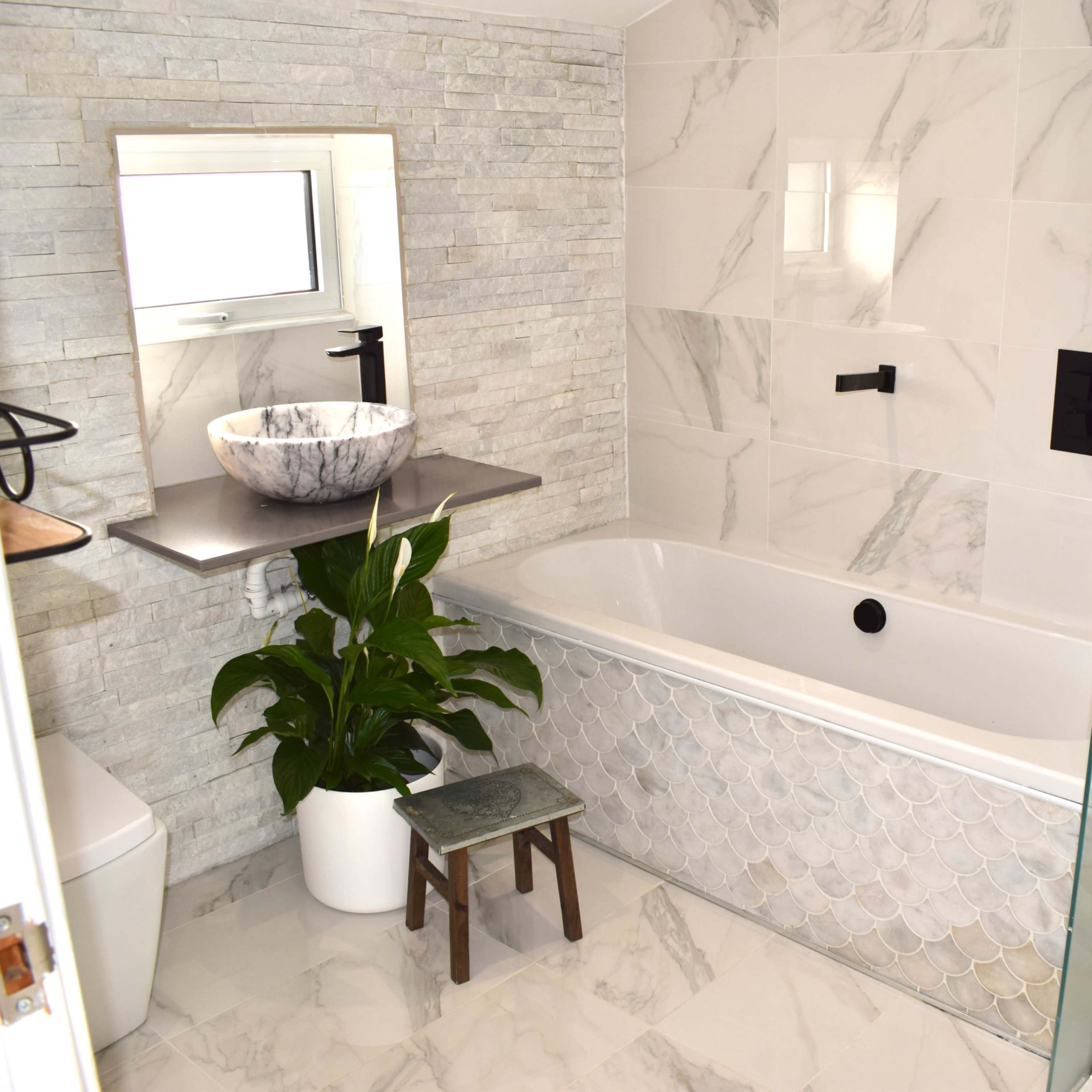 A modern bathroom featuring a freestanding bathtub, a stone sink on a floating shelf, and a potted plant beside a toilet.