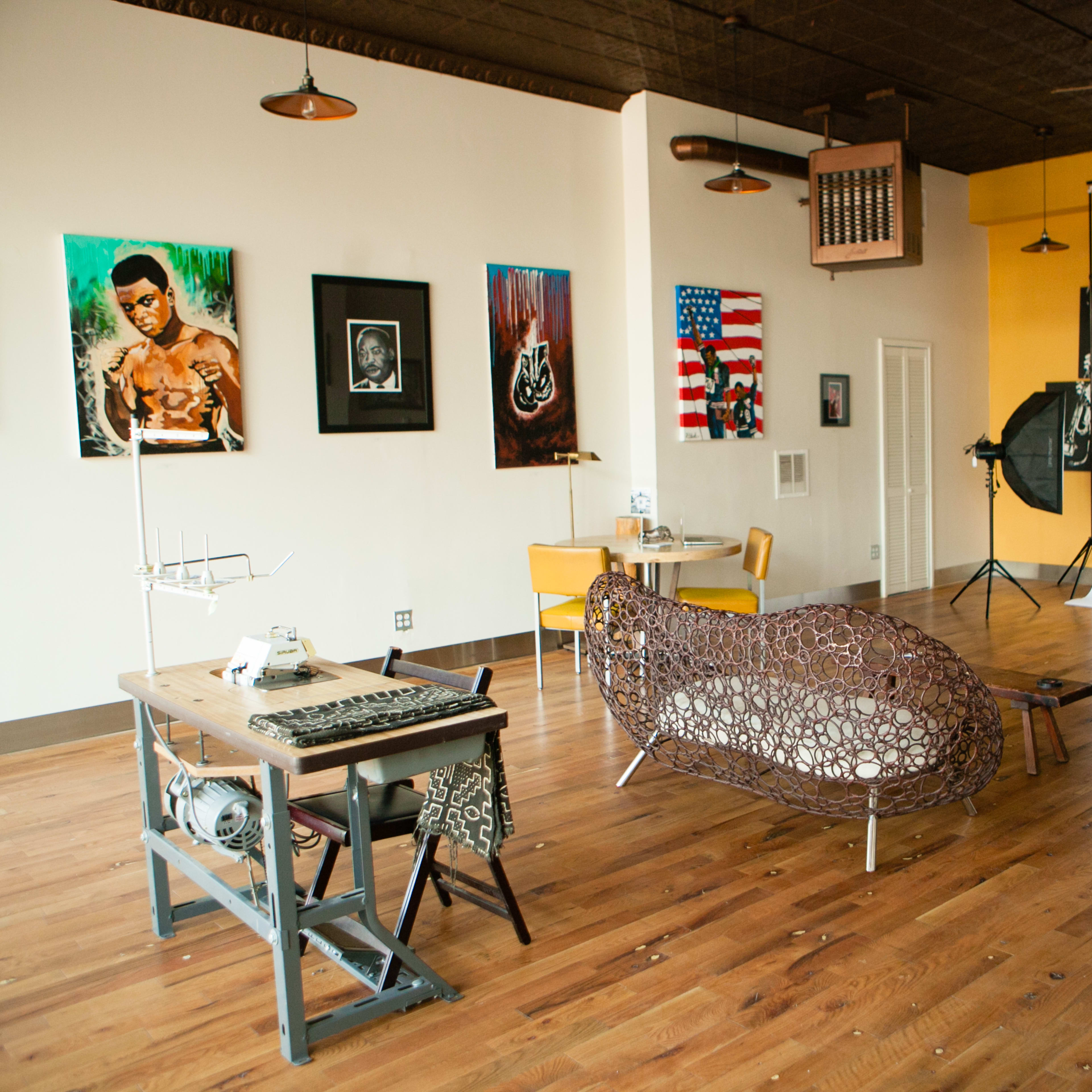 An artist studio with a wooden floor, featuring a large backdrop, photography equipment, and various artworks on the walls.