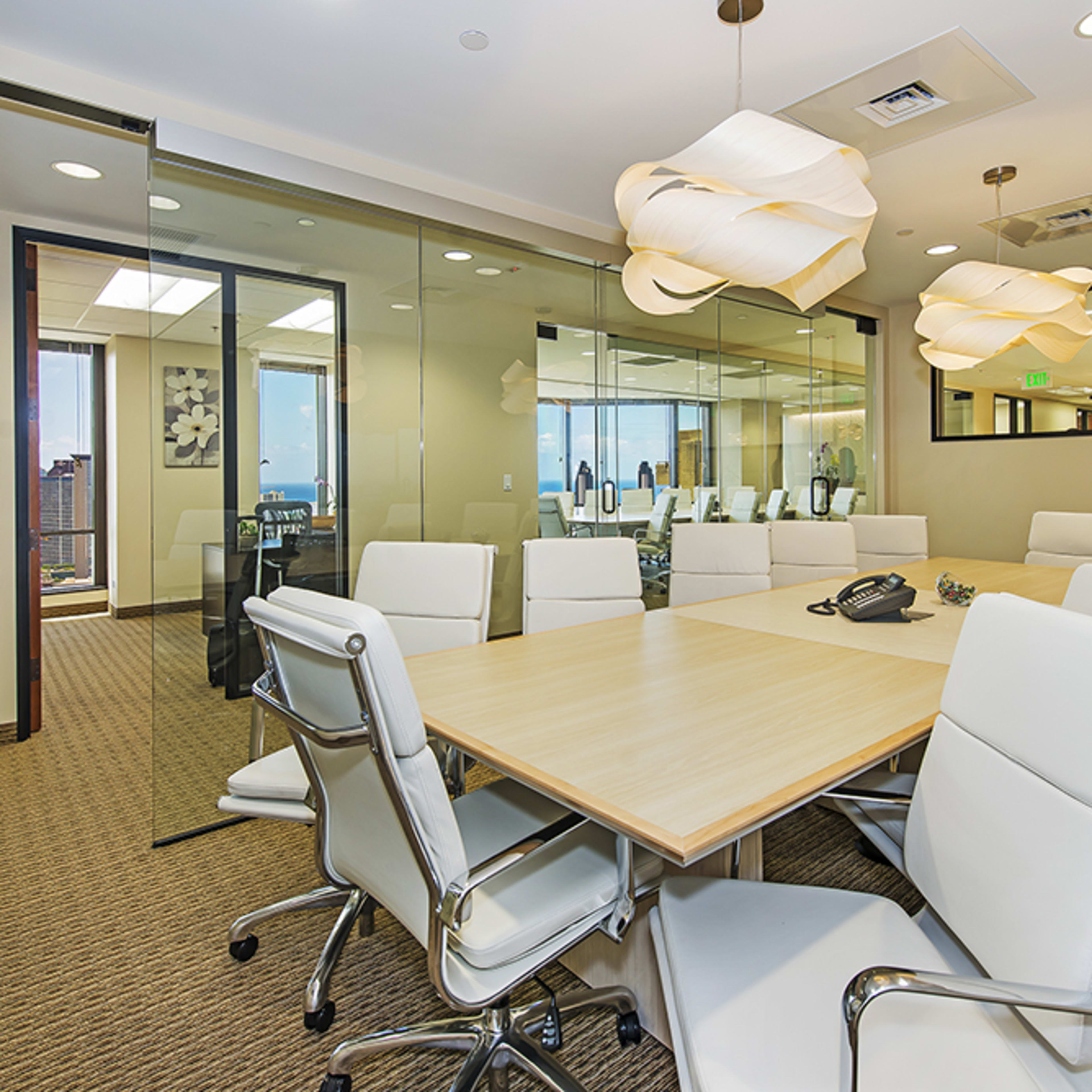 A modern conference room features a long wooden table surrounded by white ergonomic chairs, with glass walls offering views of a city skyline.