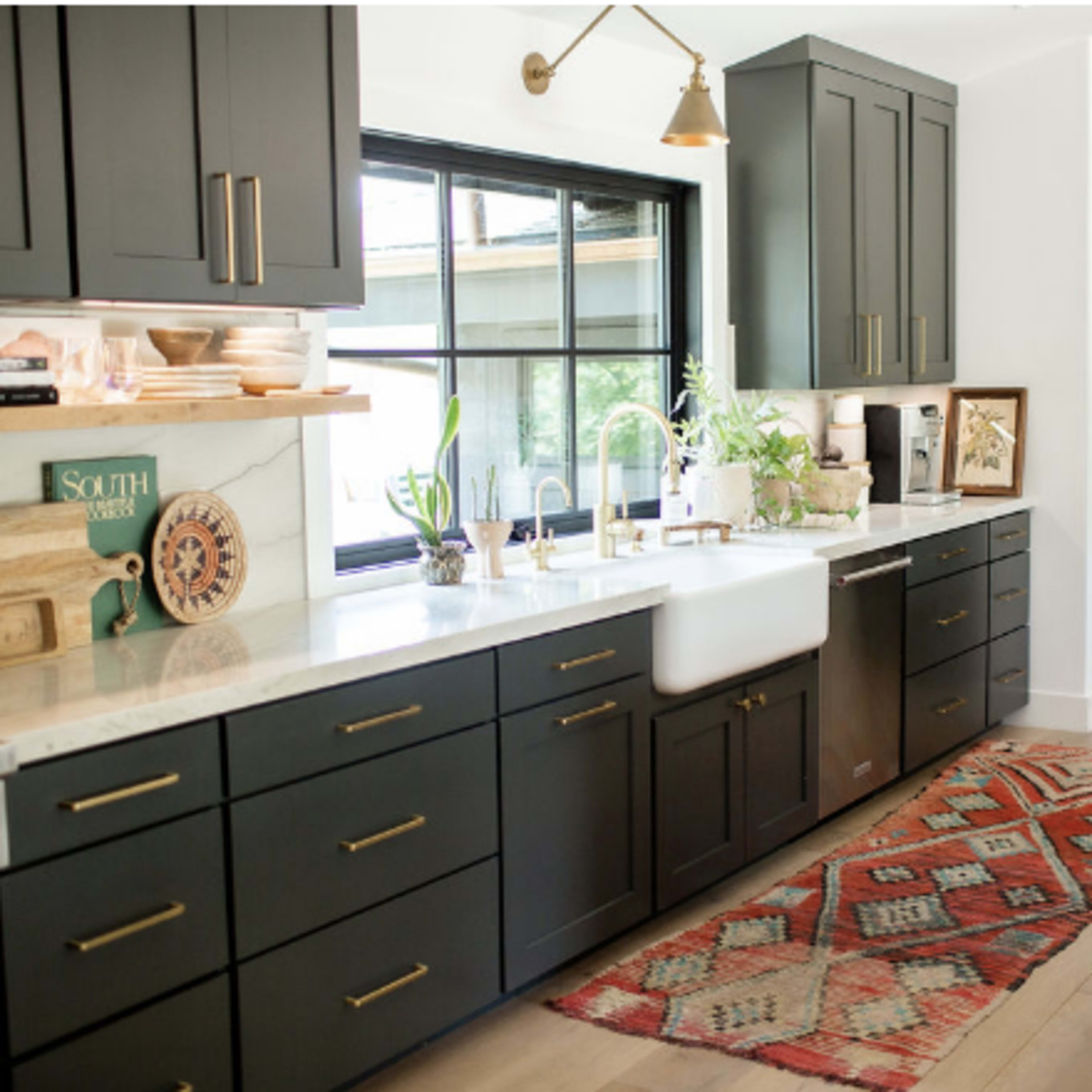 A modern kitchen features dark cabinetry, a large farmhouse sink, and a colorful area rug on the floor.