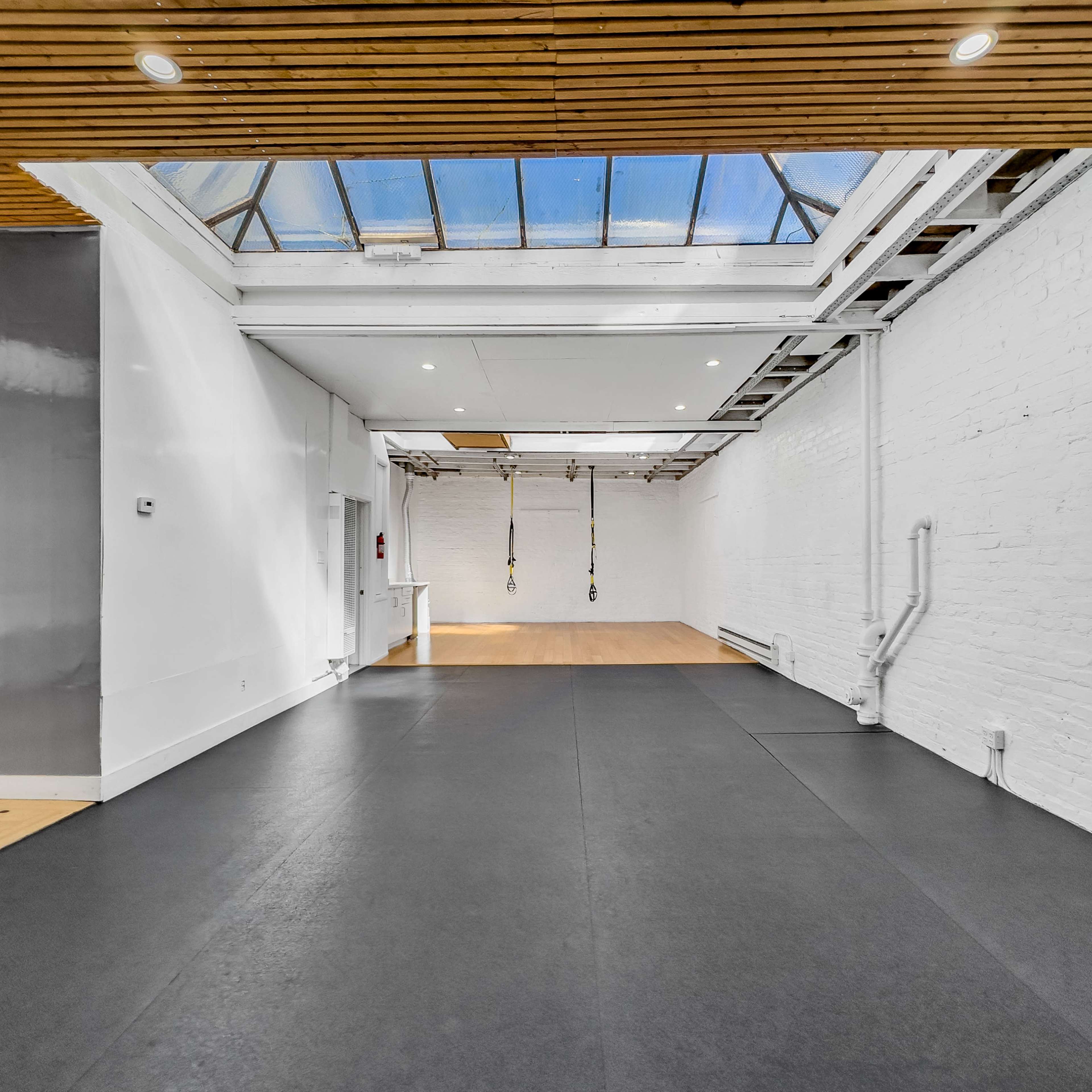 A spacious, well-lit interior room with wooden beams and a black rubber floor.