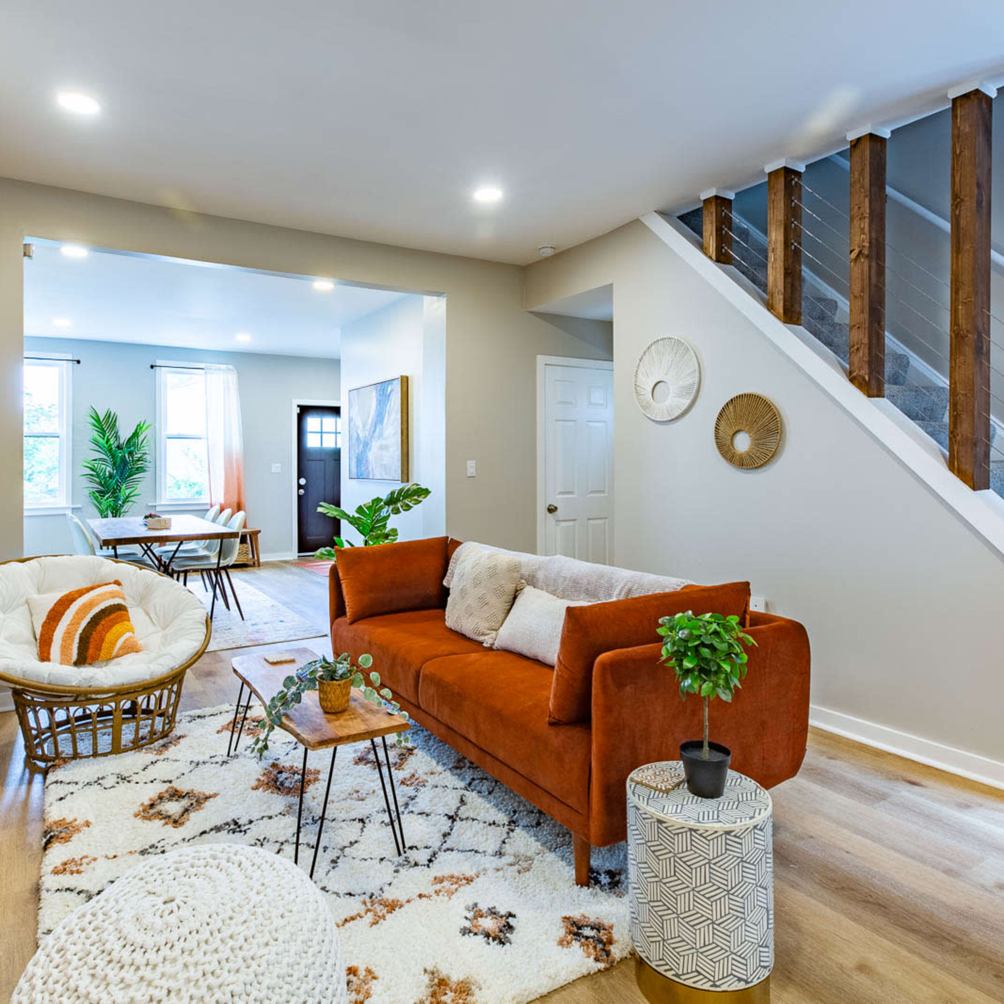 A modern living room with an orange sofa, a patterned rug, a round coffee table, and a staircase leading to an upper level.