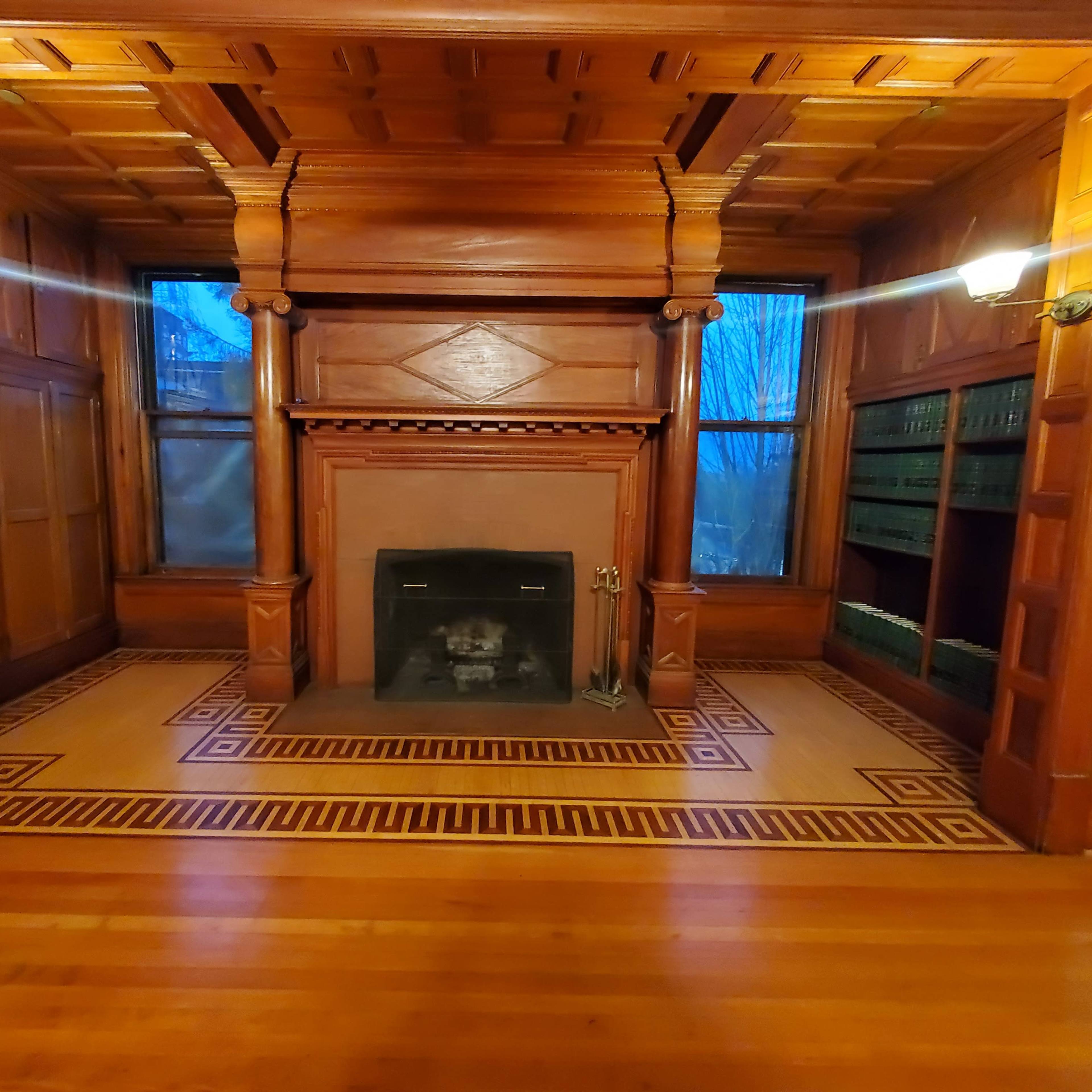 A spacious room with wooden walls, a central fireplace, and patterned tile flooring, illuminated by two wall sconces.