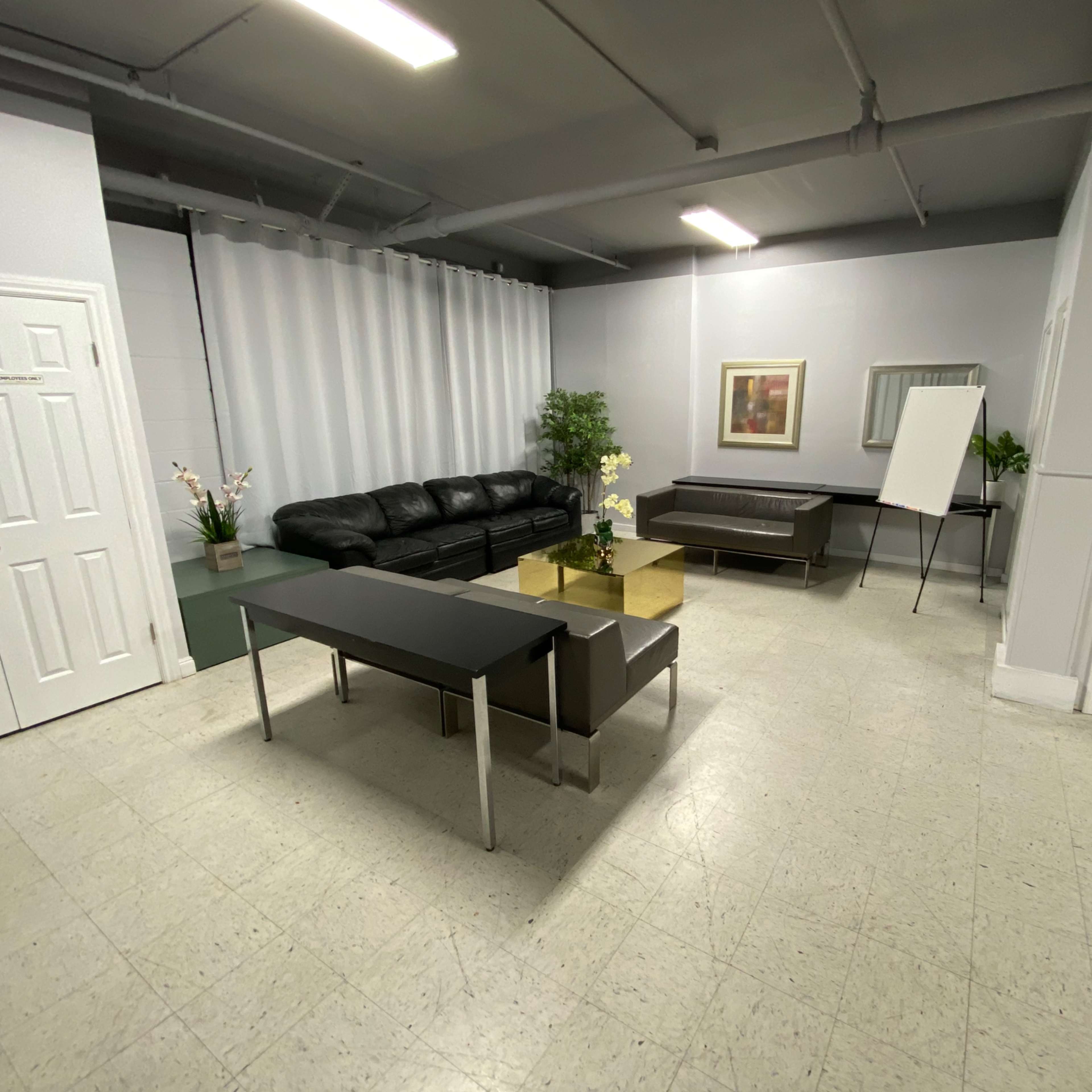 A minimalist waiting area featuring a black leather sofa, a glass coffee table, a small plant, and a whiteboard on an easel.