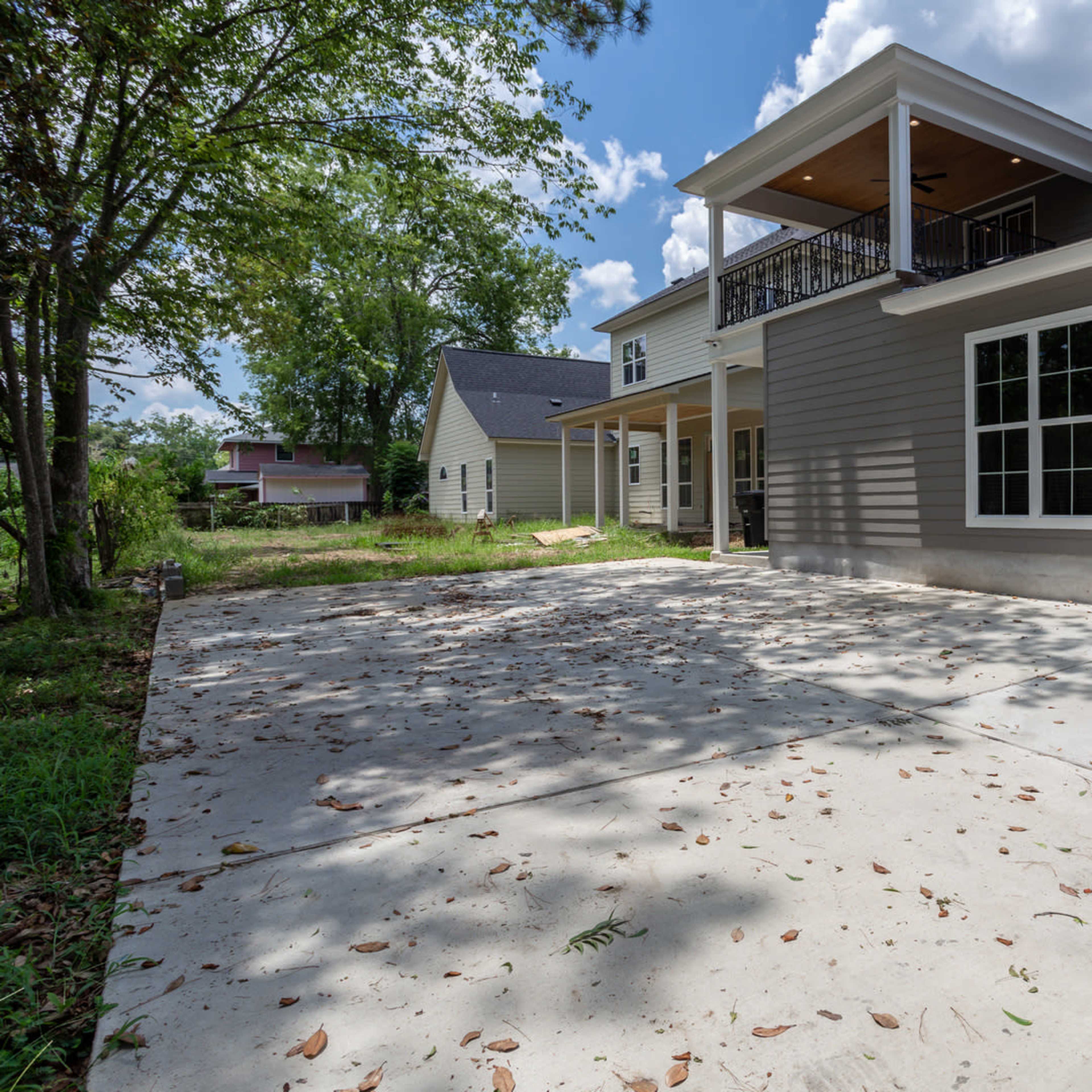 A newly constructed two-story house with a concrete driveway, surrounded by trees and a grassy area.