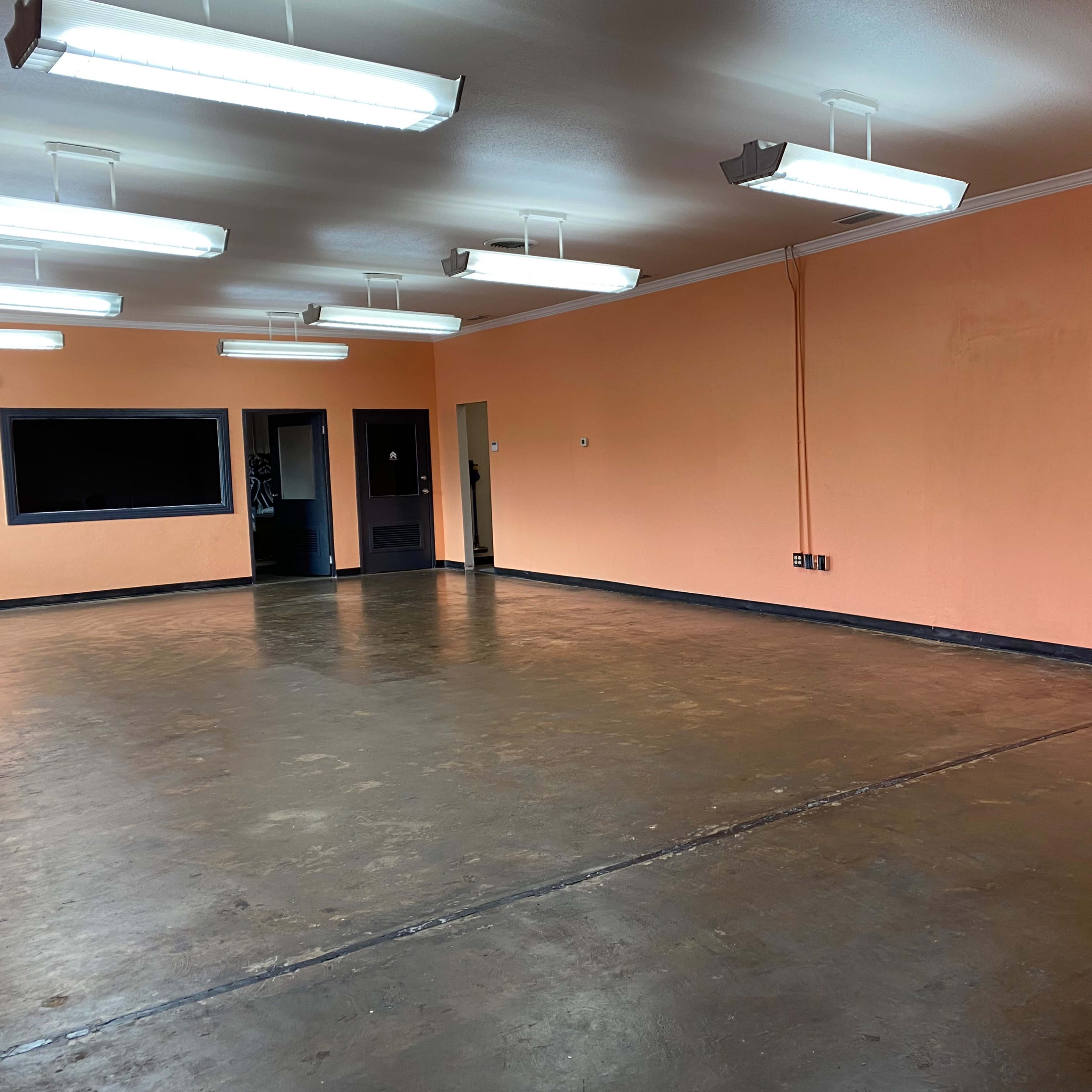 A spacious room with a polished concrete floor, orange walls, and fluorescent lighting.