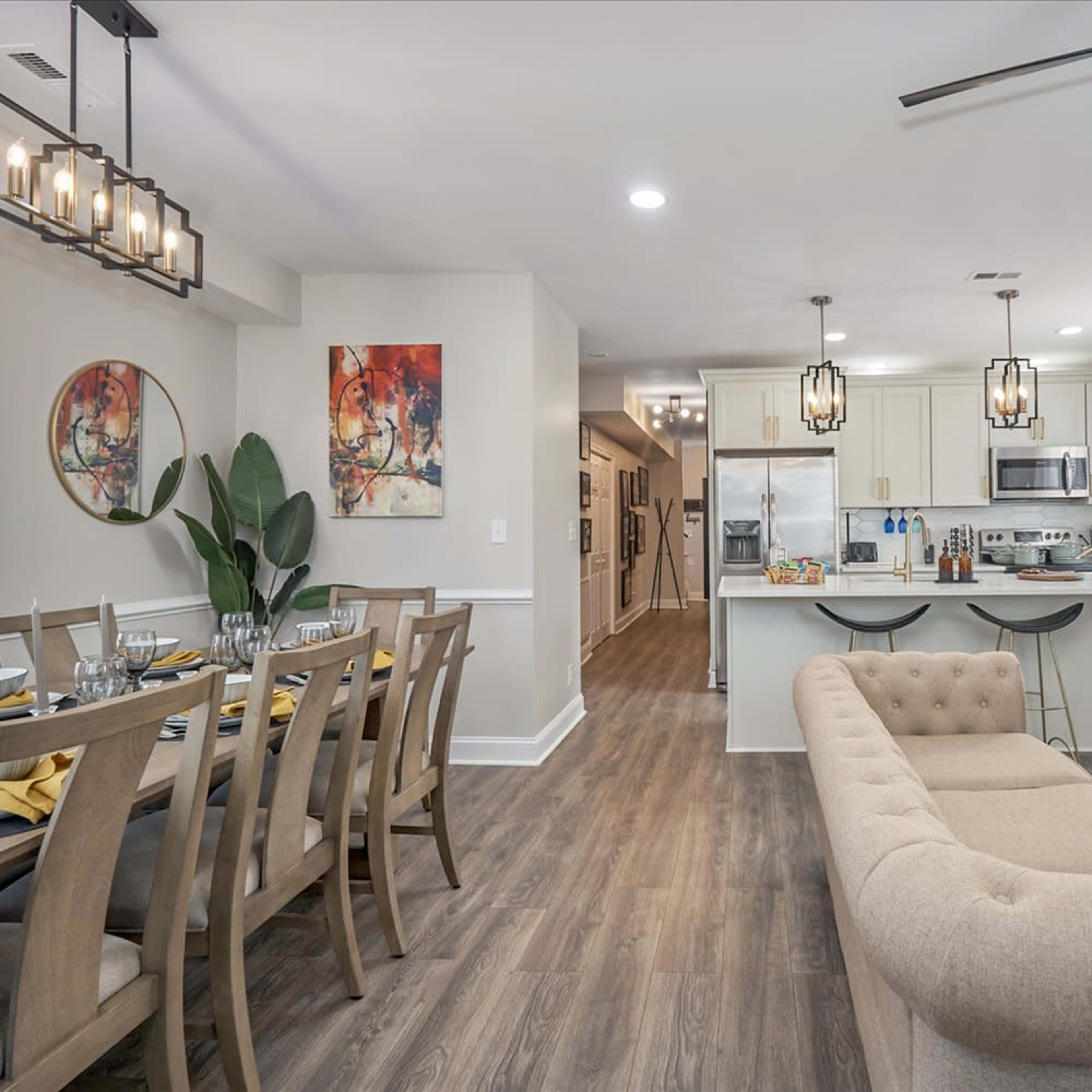 A modern open-concept living and dining area with a beige couch, a dining table set for meals, and a kitchen in the background.