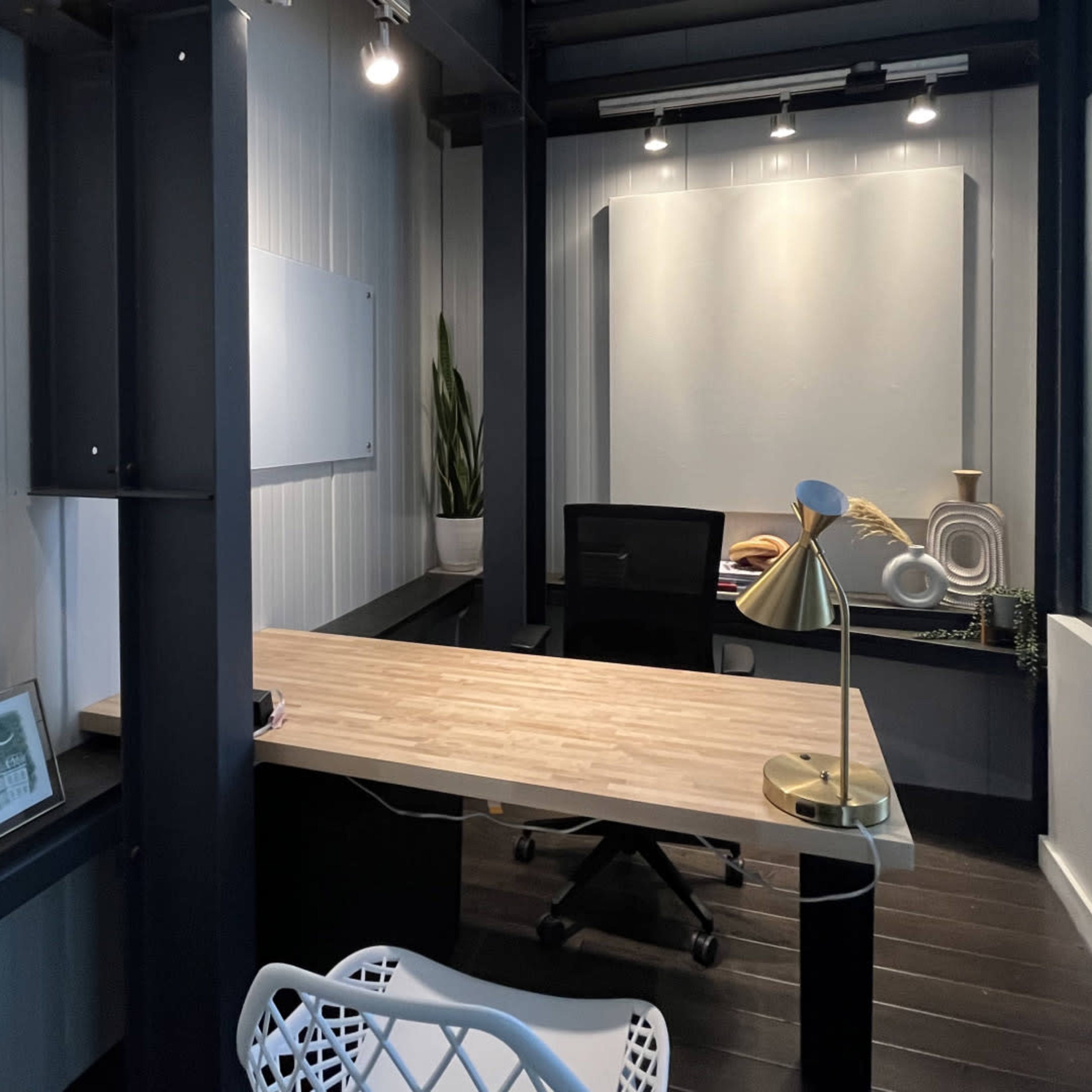 A modern office space with a wooden desk, a black office chair, and decorative elements, featuring minimalist design details and ample lighting.
