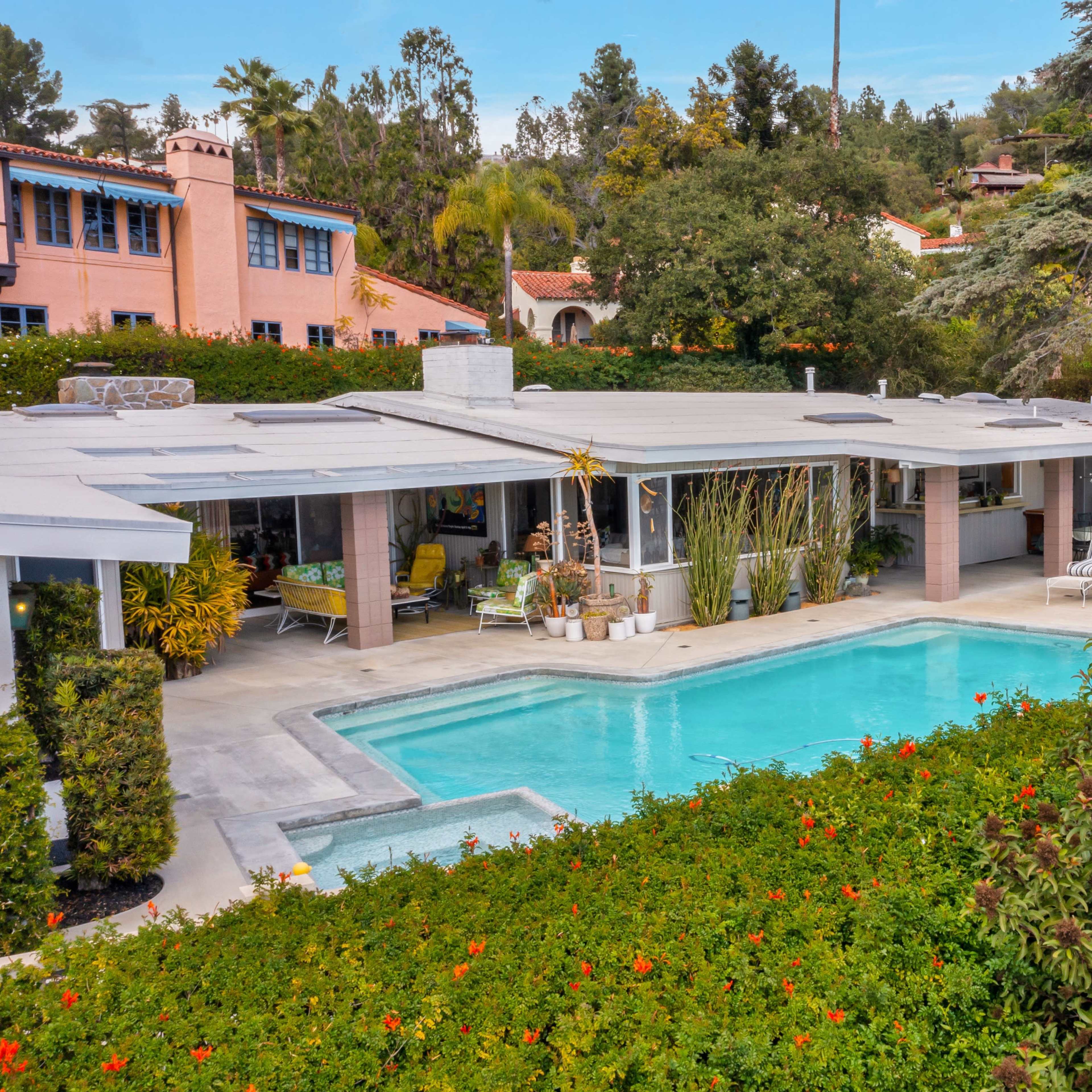 A modern home with a swimming pool surrounded by lush greenery and flowering plants.