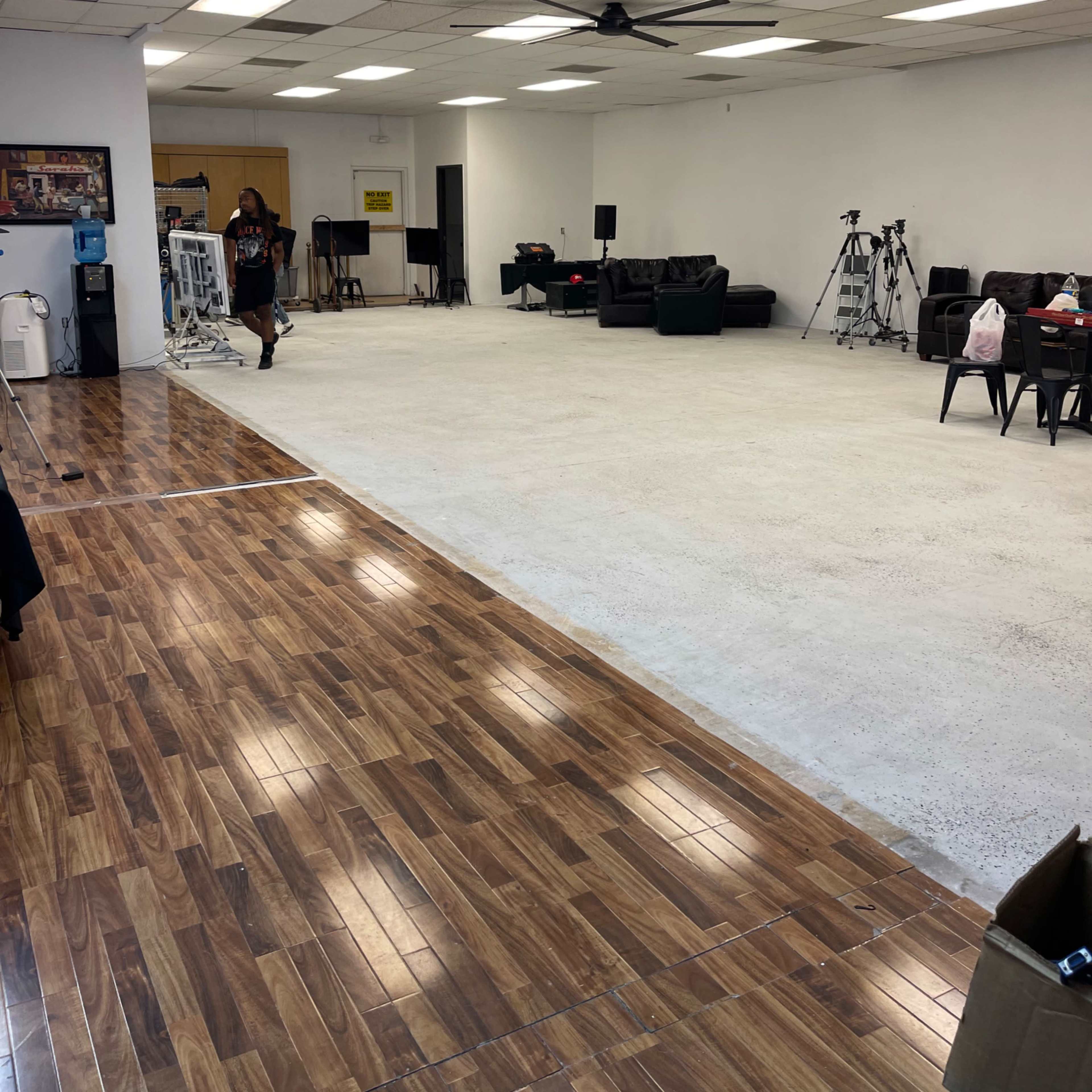 A spacious room with a smooth concrete floor, a section of wooden flooring, a few couches, and several cameras set up along one wall.