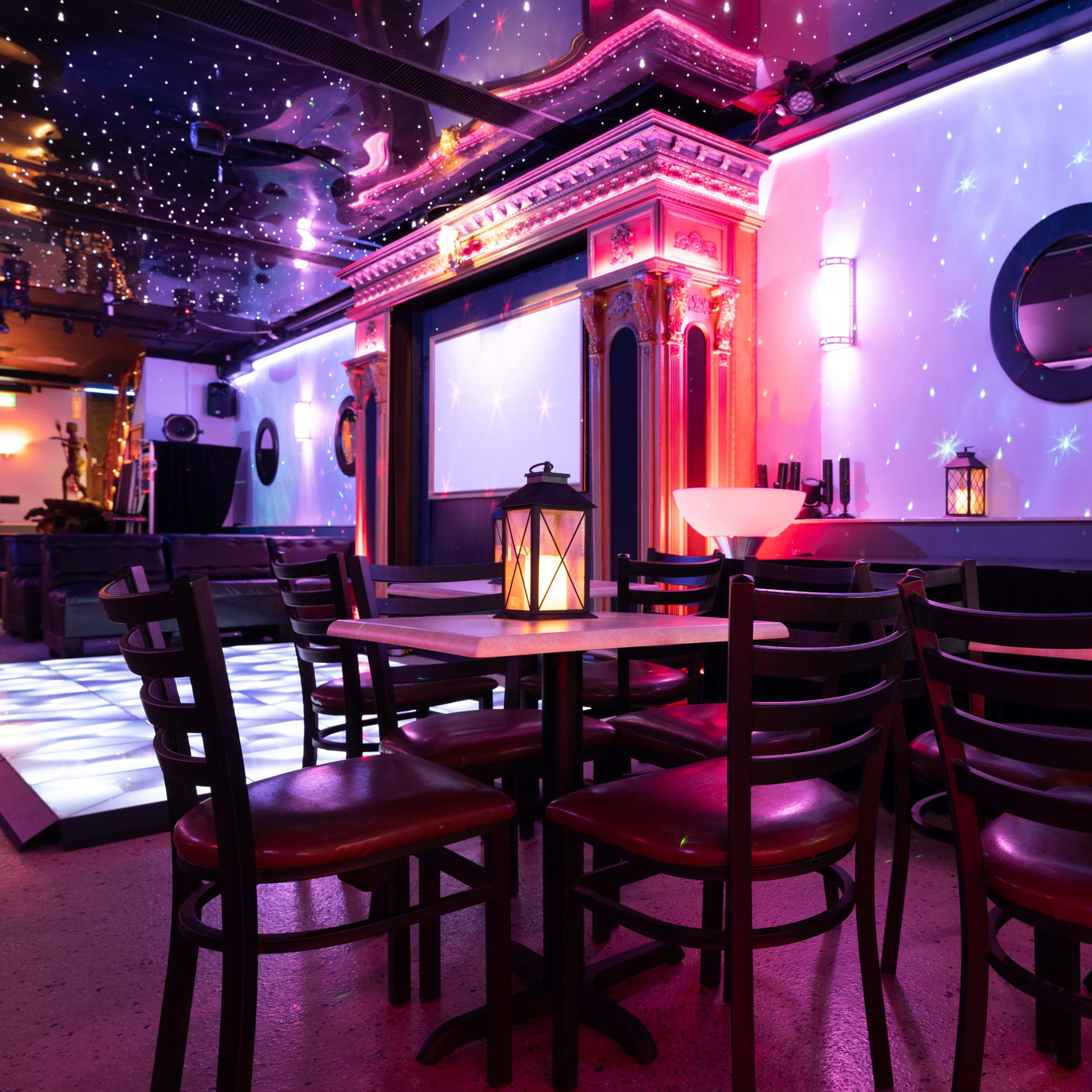 A cozy event space features tables with lanterns, a stage adorned with colorful lighting, and a ceiling resembling a starry night.