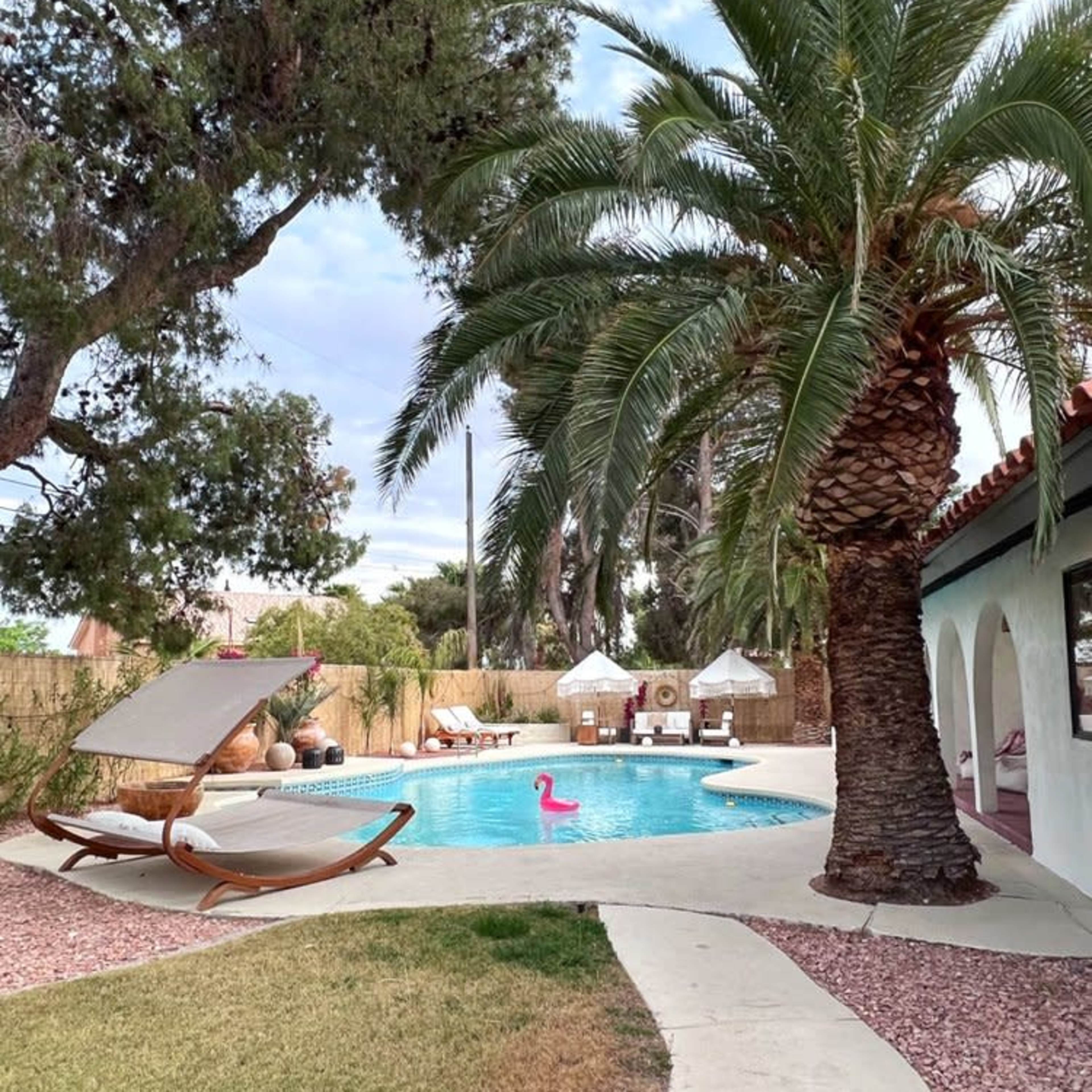 A pool area features a palm tree, lounge chairs, and a pink flamingo float, surrounded by landscaped grass and pathways.