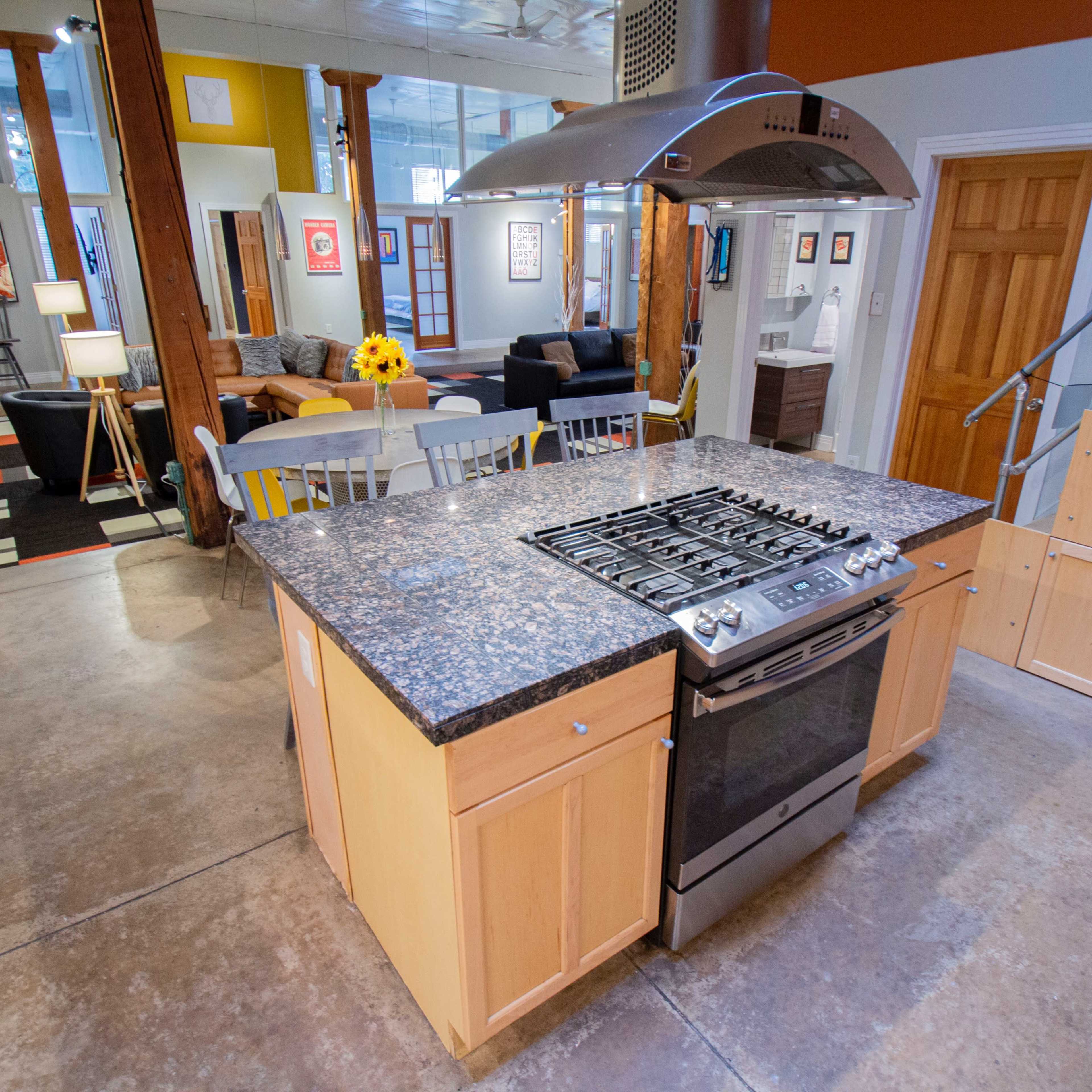 A modern kitchen with a central island, gas stove, and stainless steel appliances, leading into a living area with wooden beams and a separated seating space.