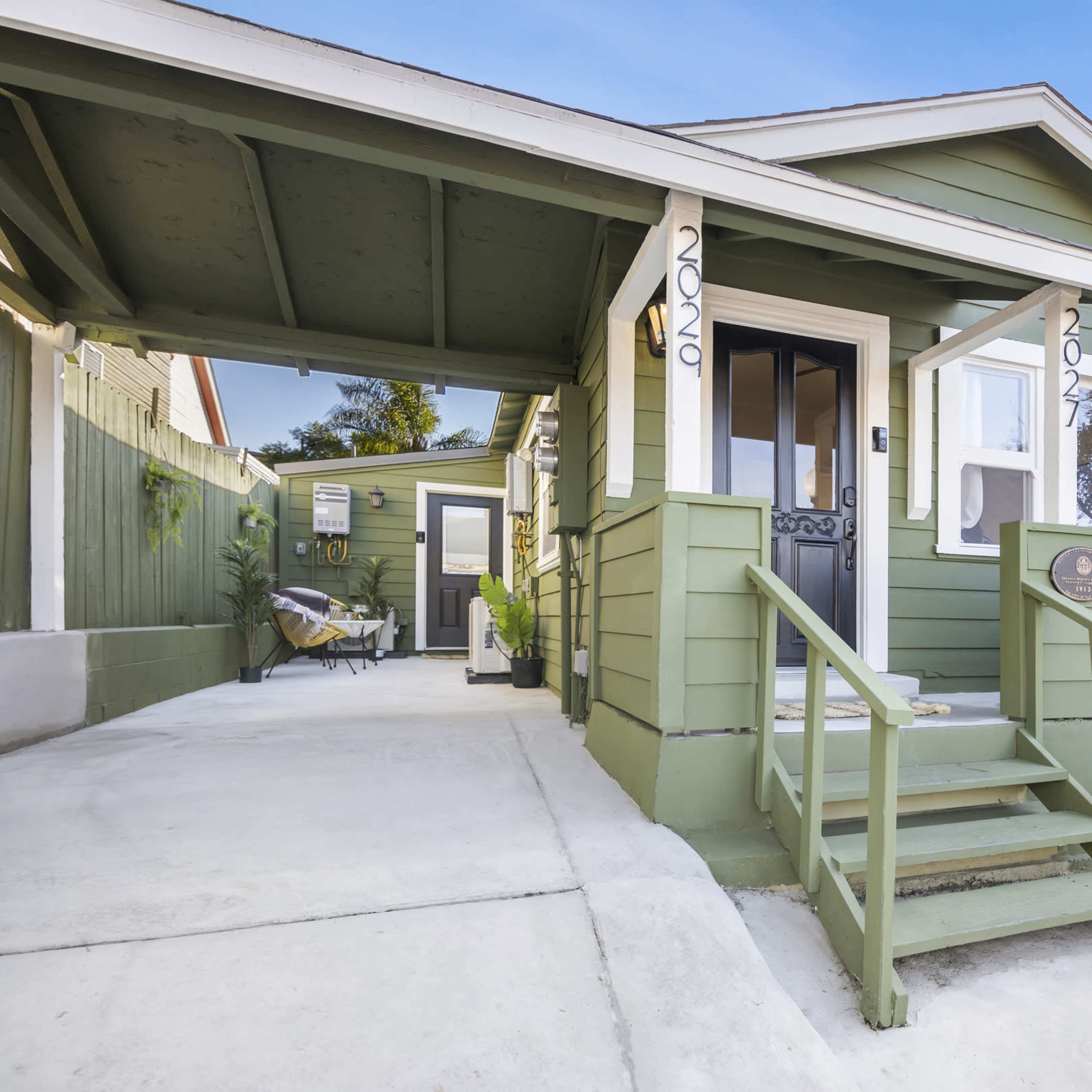 A green house with a covered porch and stairs leading up to the front door, situated on a clear day.