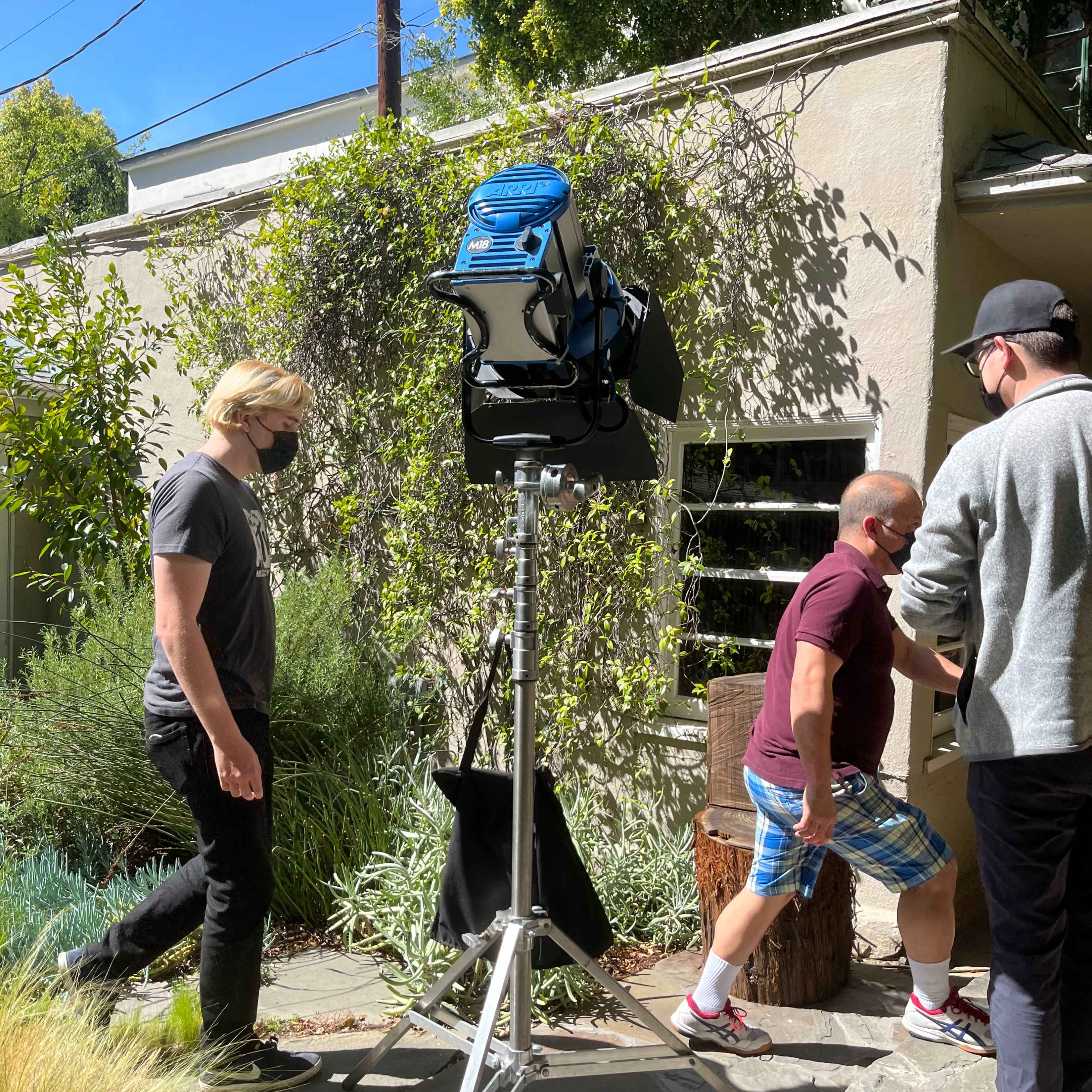 A portable floodlight is set up next to a pathway while two individuals walk in front of it.