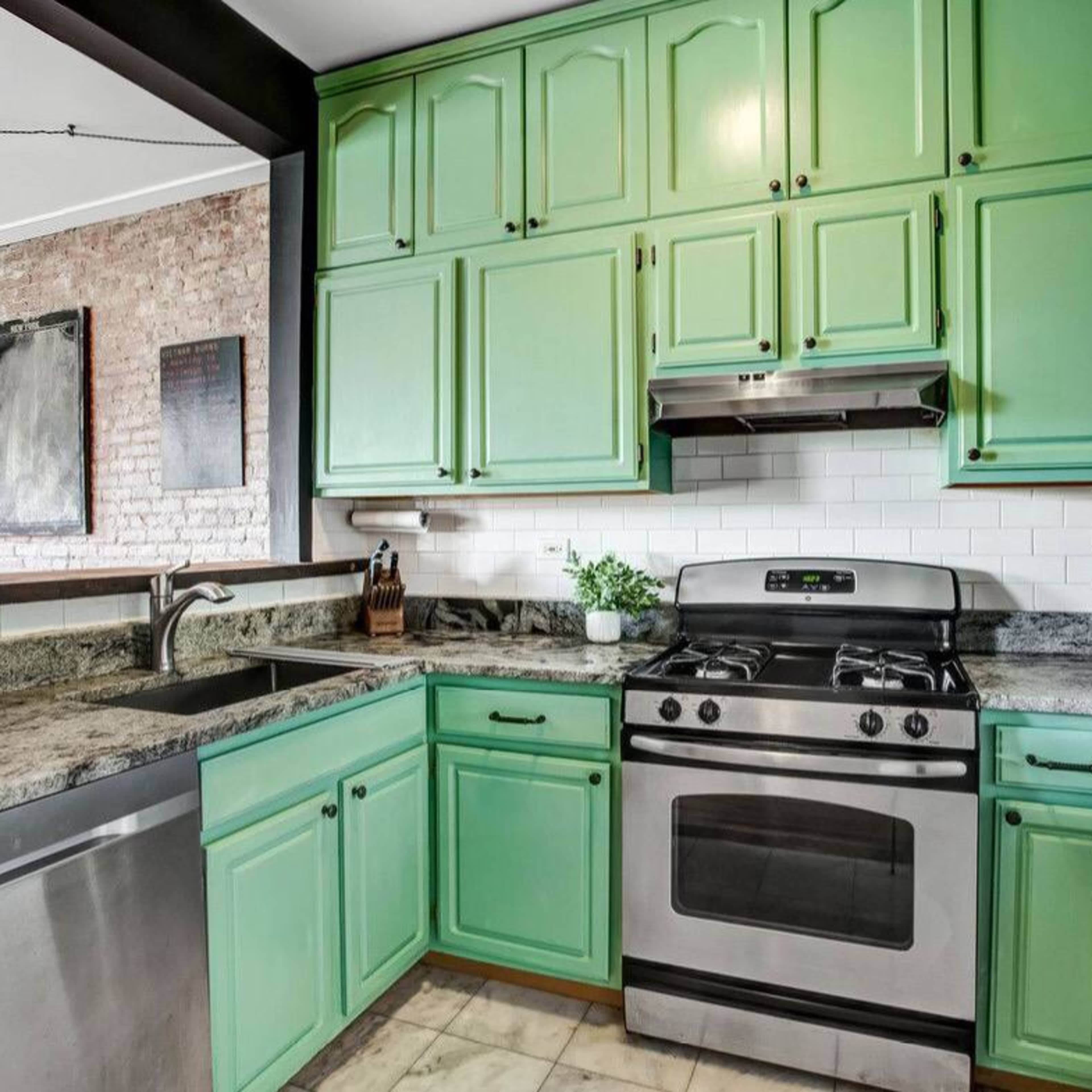 A kitchen featuring mint green cabinets, stainless steel appliances, and a granite countertop with a sink.