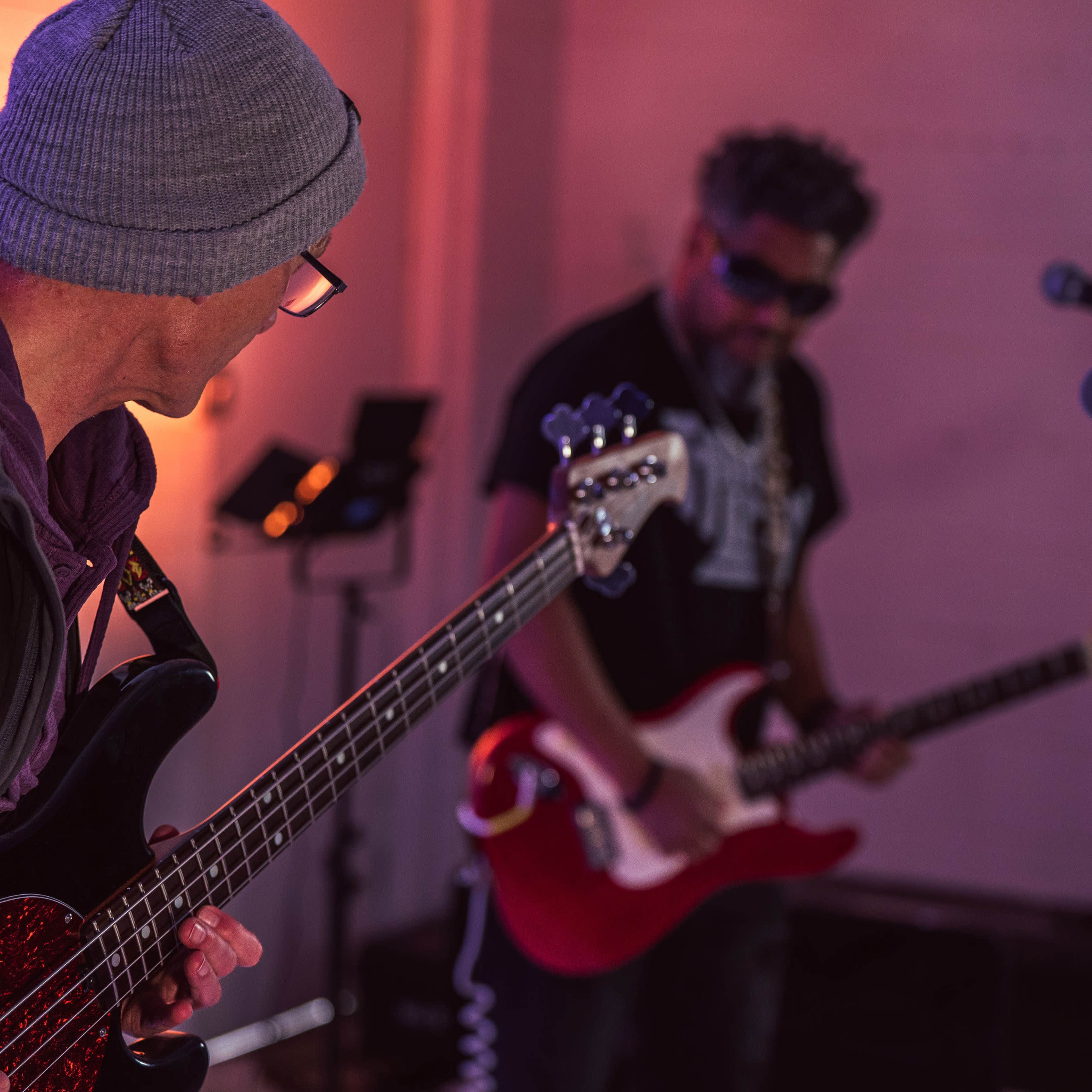 Two musicians perform in a studio, with one playing an electric bass and the other an electric guitar.