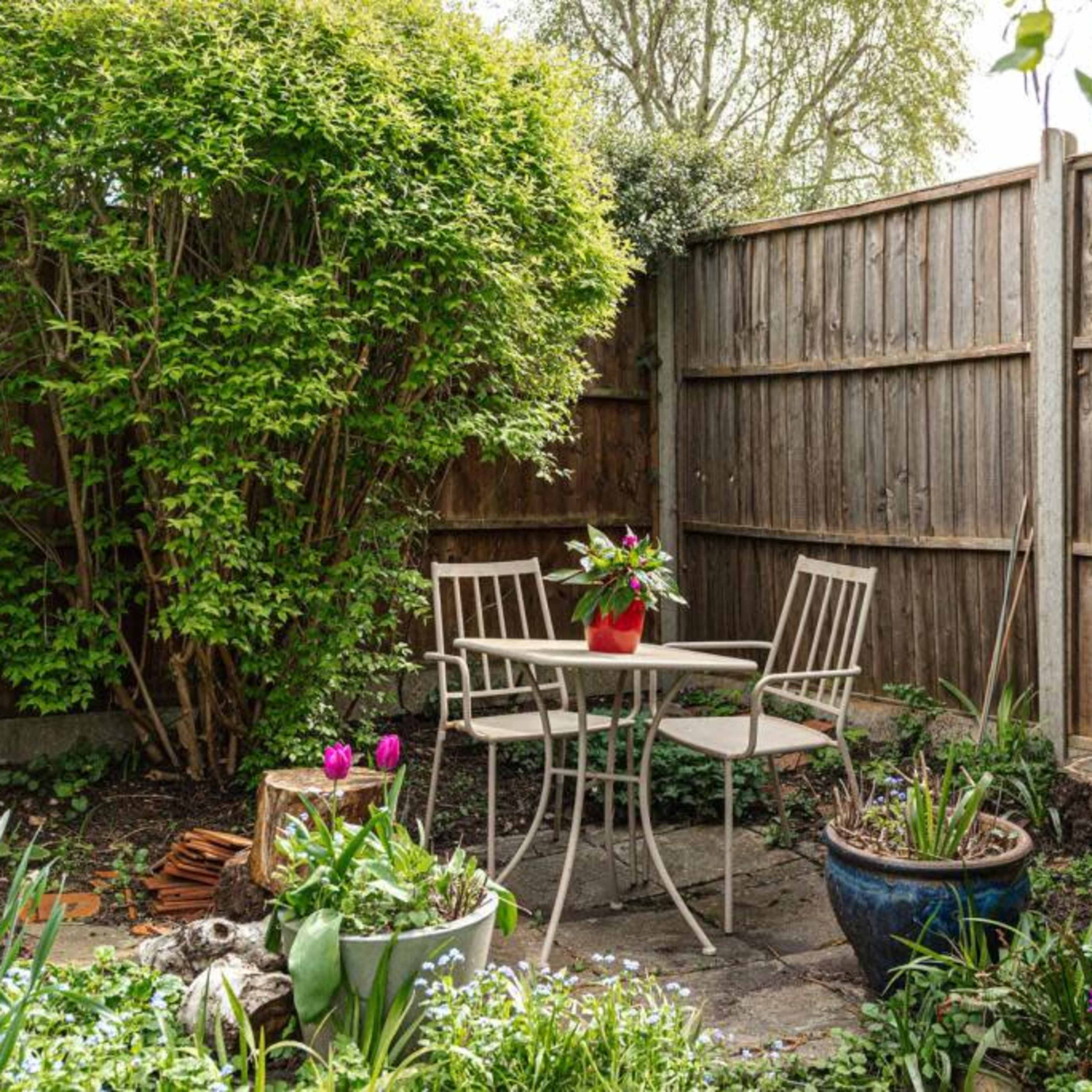 A small garden area with a table and two chairs surrounded by lush greenery and flowering plants.