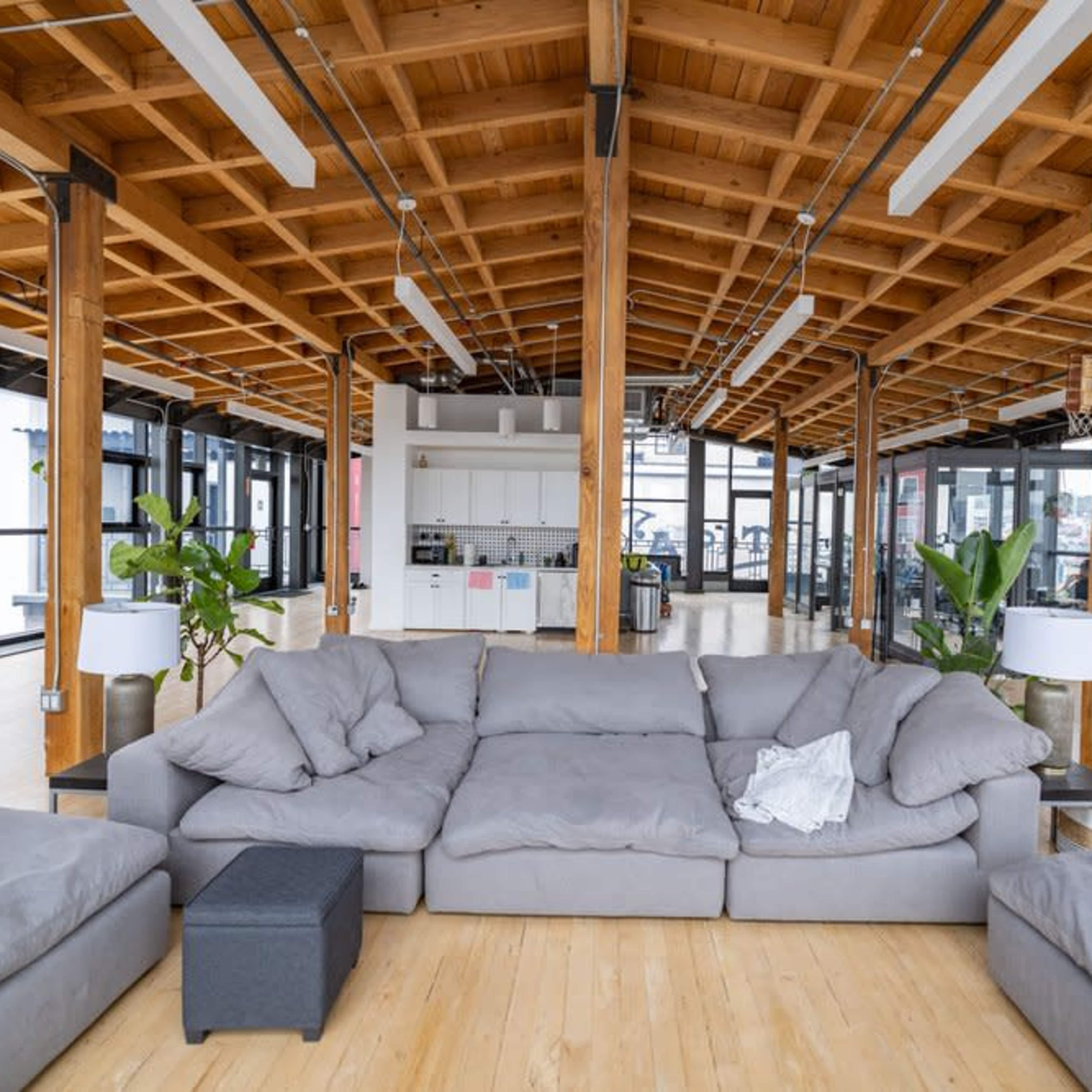 A spacious, modern office interior with a large, gray sectional sofa in the foreground and large windows providing natural light.