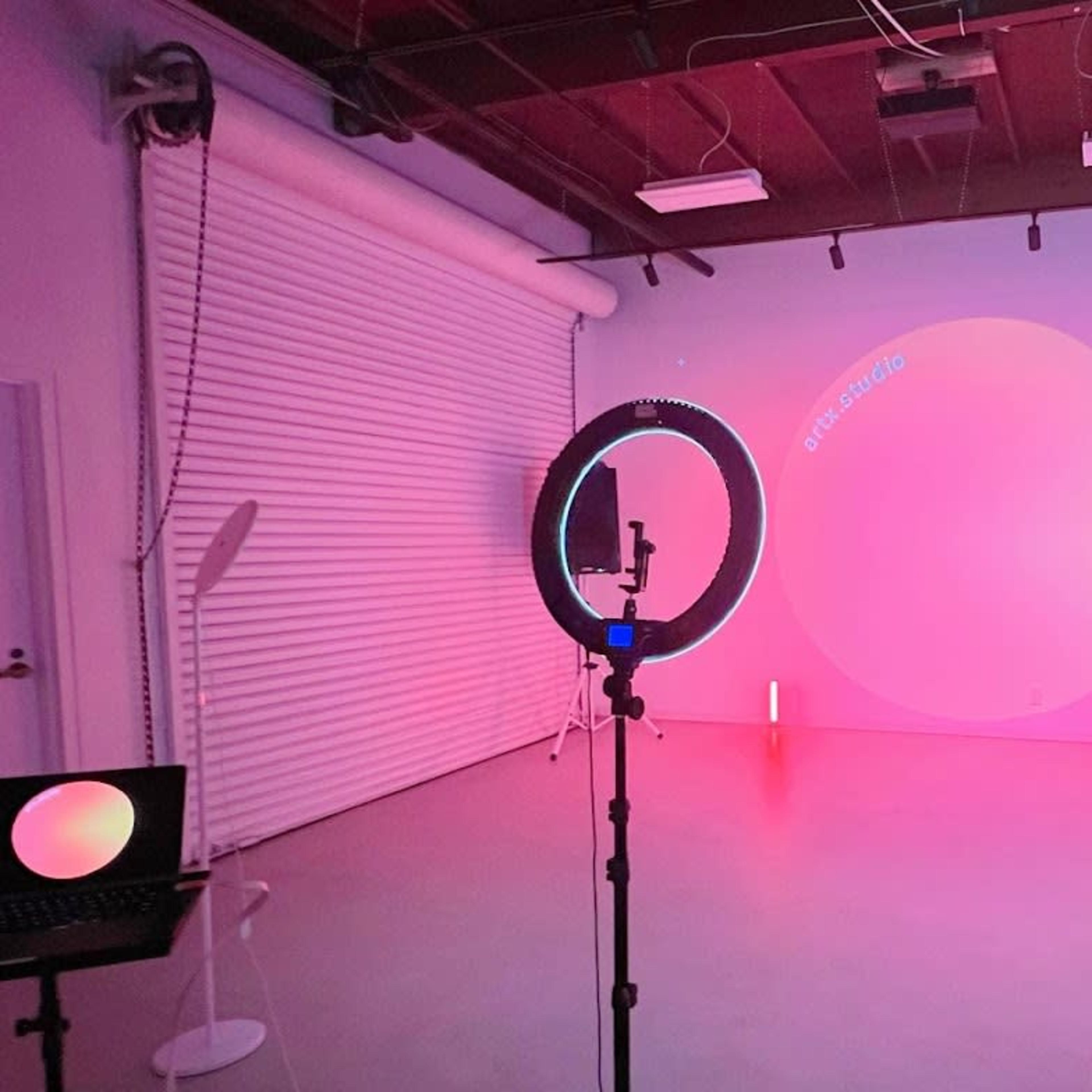 A photography studio illuminated with pink and purple lighting, featuring a circular backdrop and various lighting equipment.