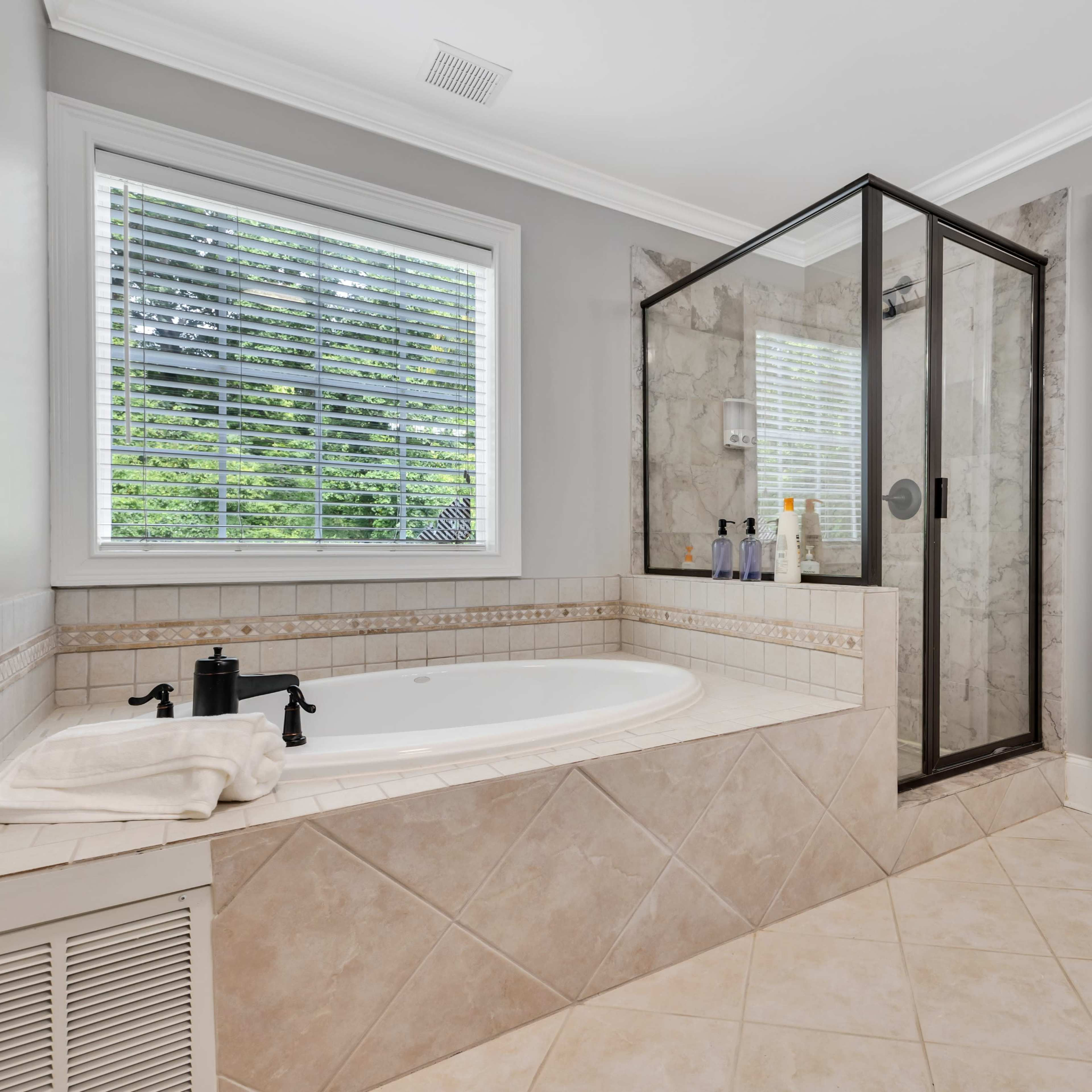A bathroom featuring a corner bathtub, a glass-enclosed shower, and a window with blinds.