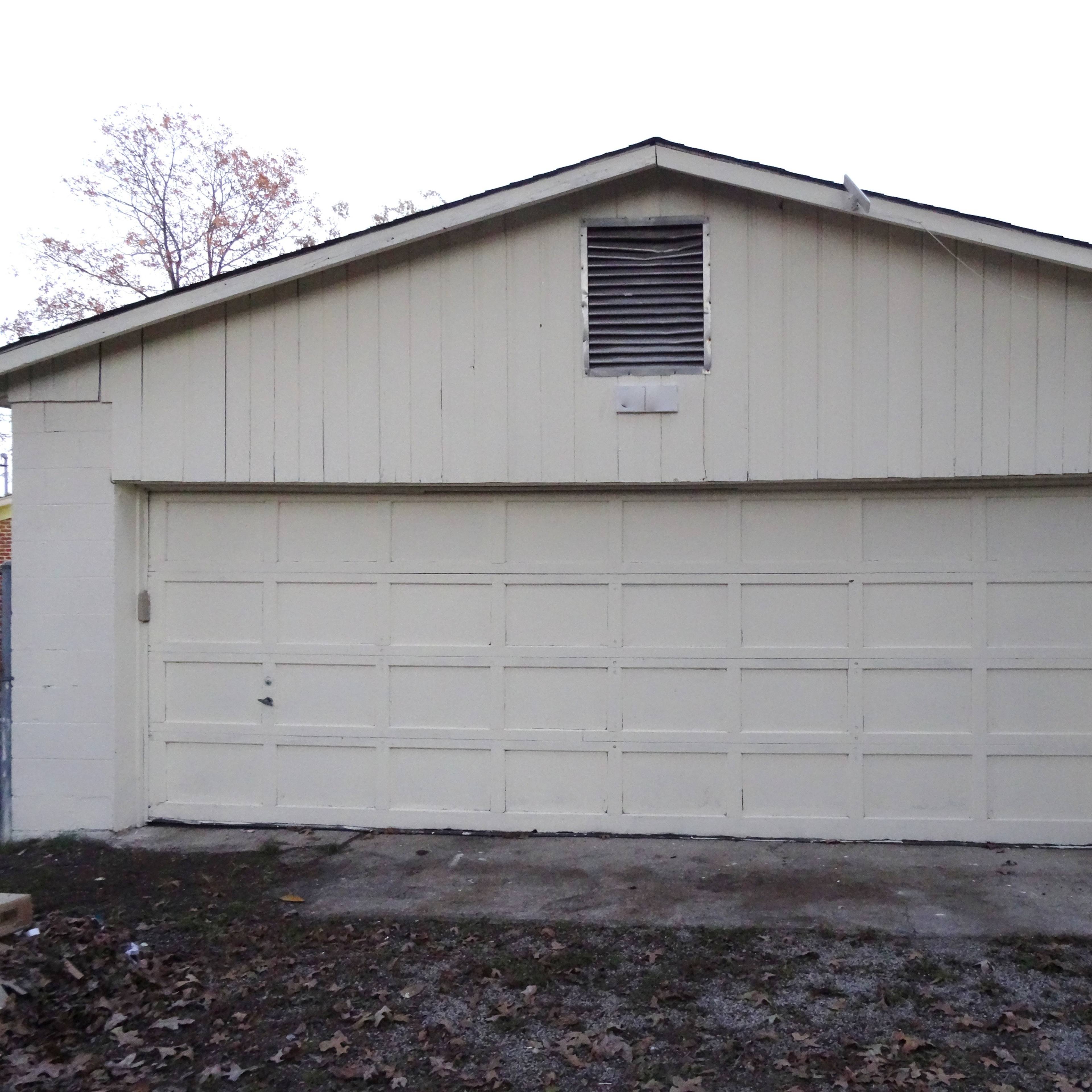 A large, beige garage with a double door and a vent is situated on a concrete slab.