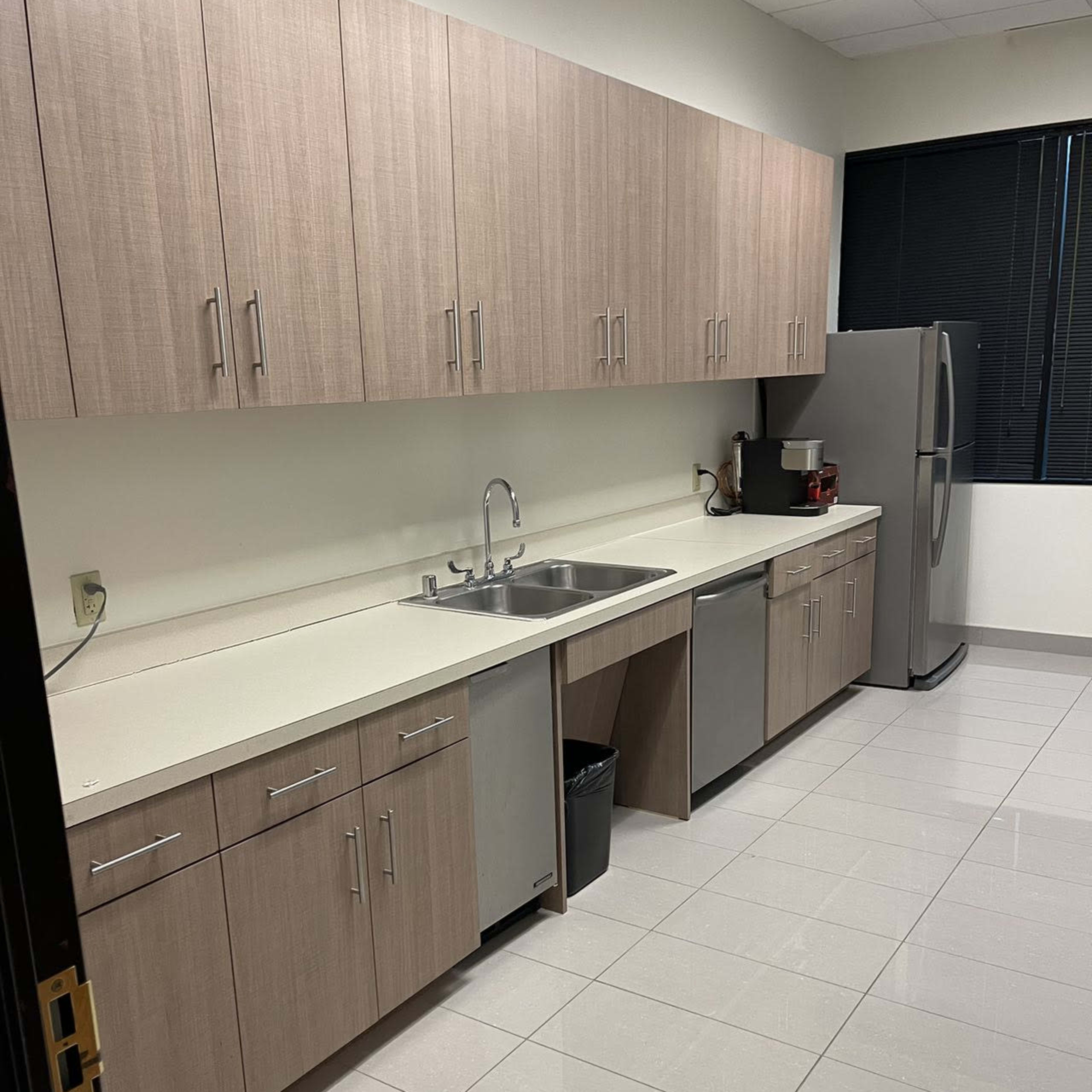 A modern kitchen with beige cabinetry, a sink, stainless steel appliances, and a tiled floor.