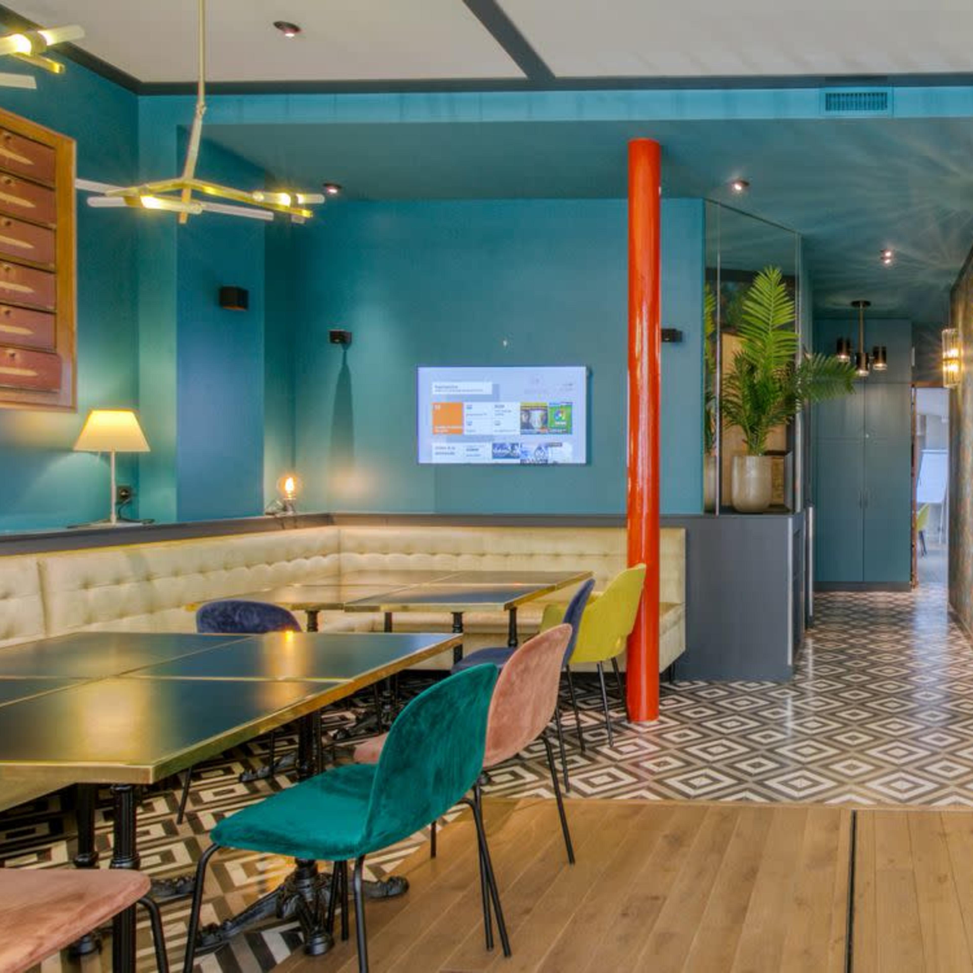 A modern restaurant interior featuring colorful furniture, a bar area with unique stools, and geometric tile flooring.