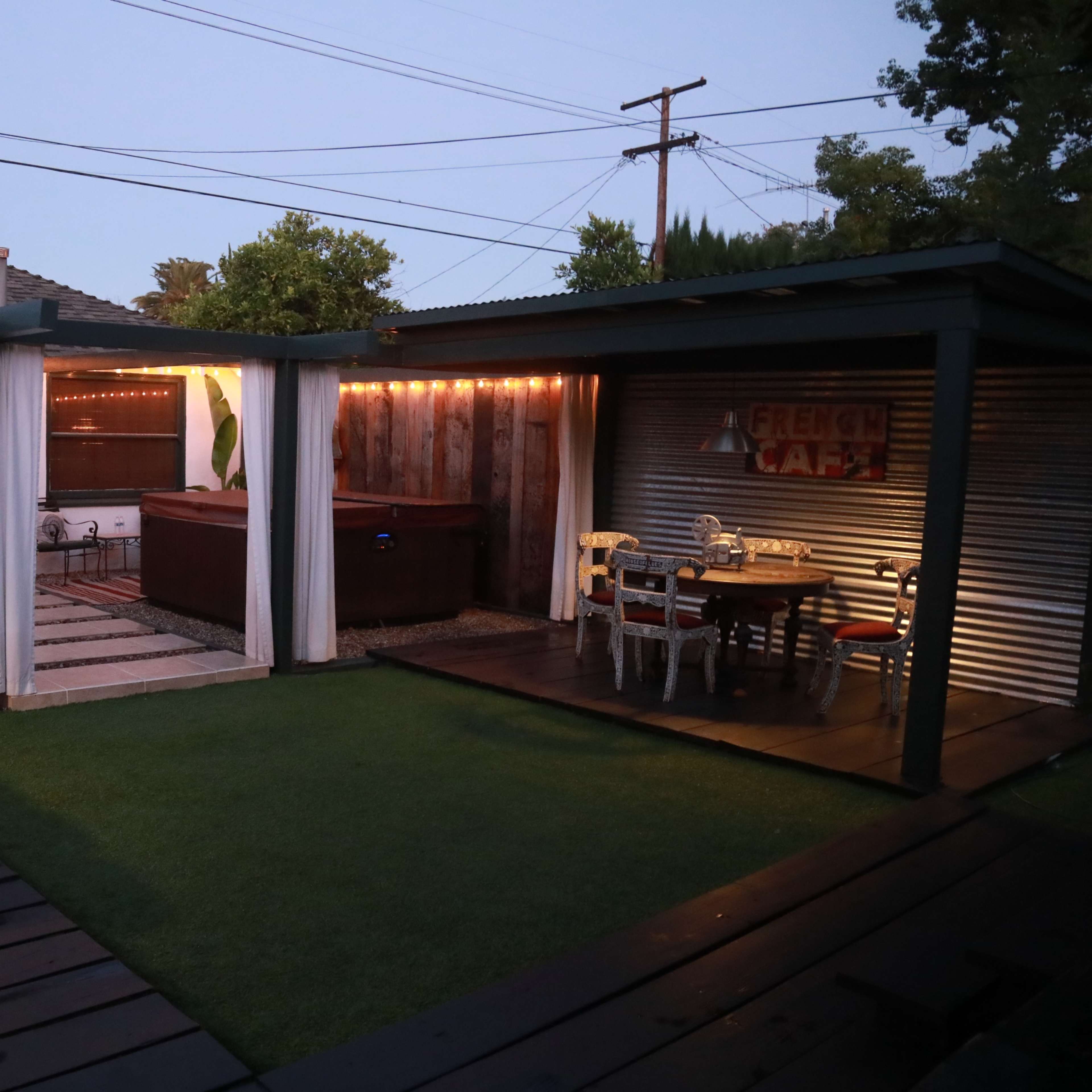 A dimly lit outdoor patio area with seating, a hot tub, and decorative elements under a clear evening sky.
