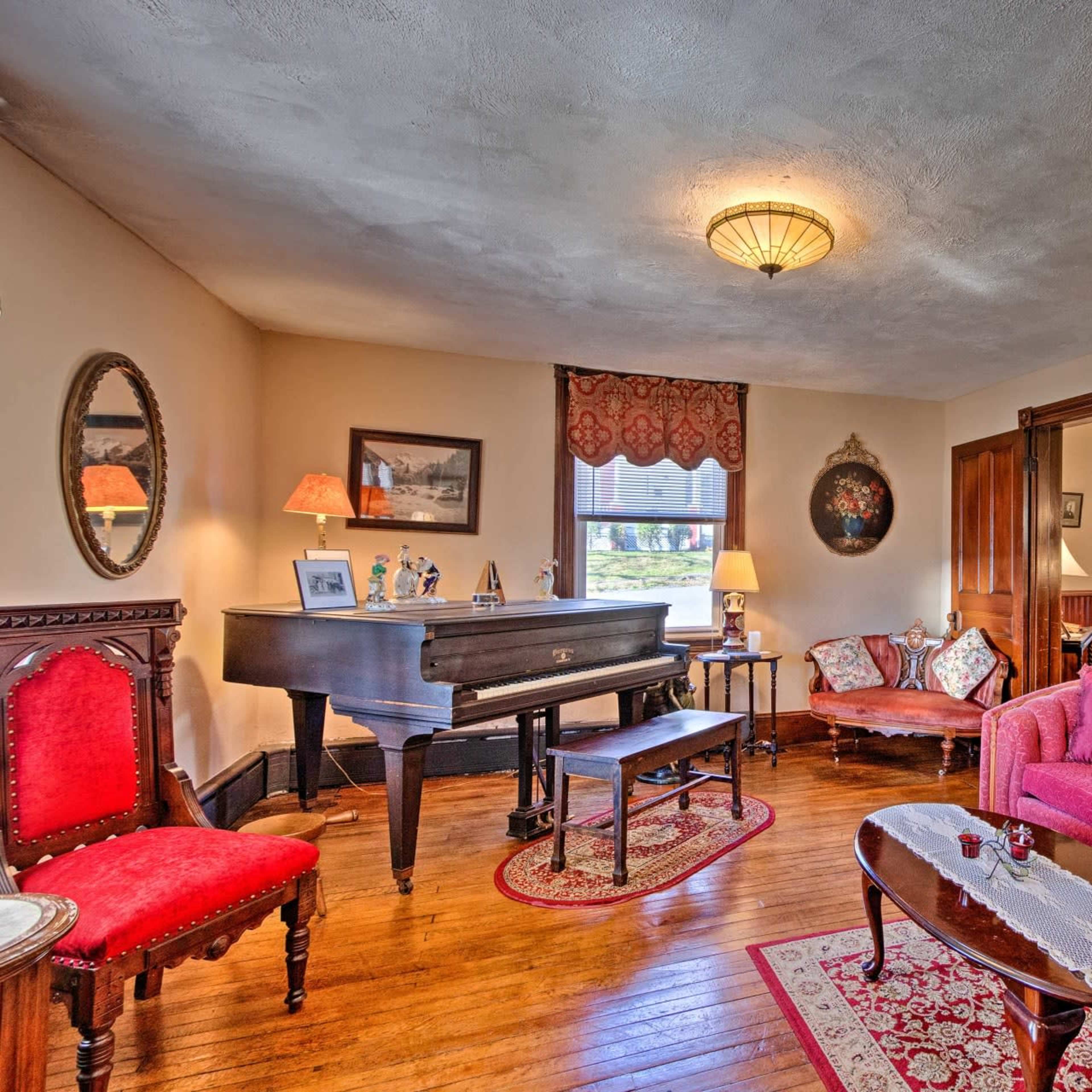 The living room features a grand piano, vintage furniture, and decorative mirrors, creating a cozy gathering space.