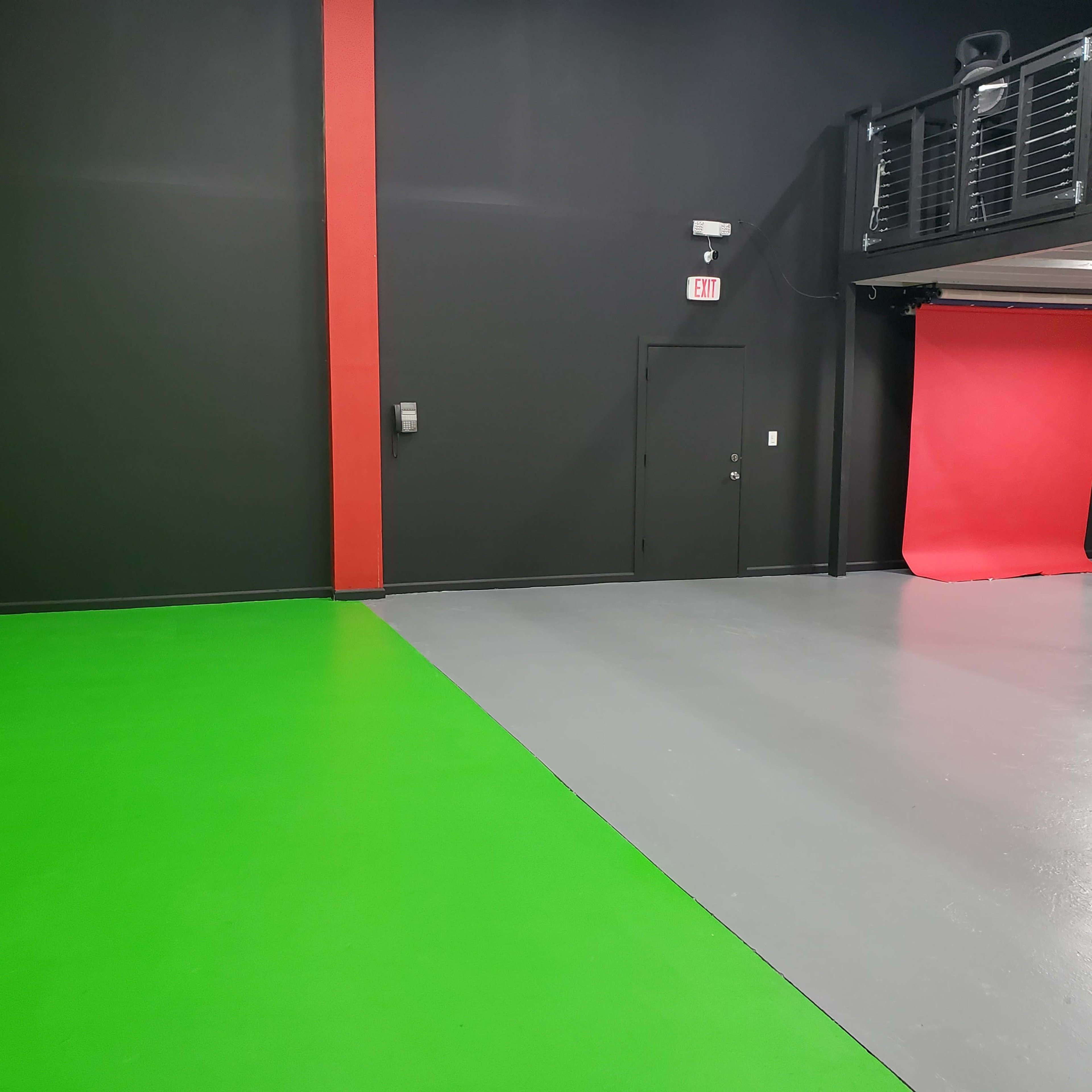 A studio space with a green wall on one side, a gray floor, and a red backdrop at the far end.