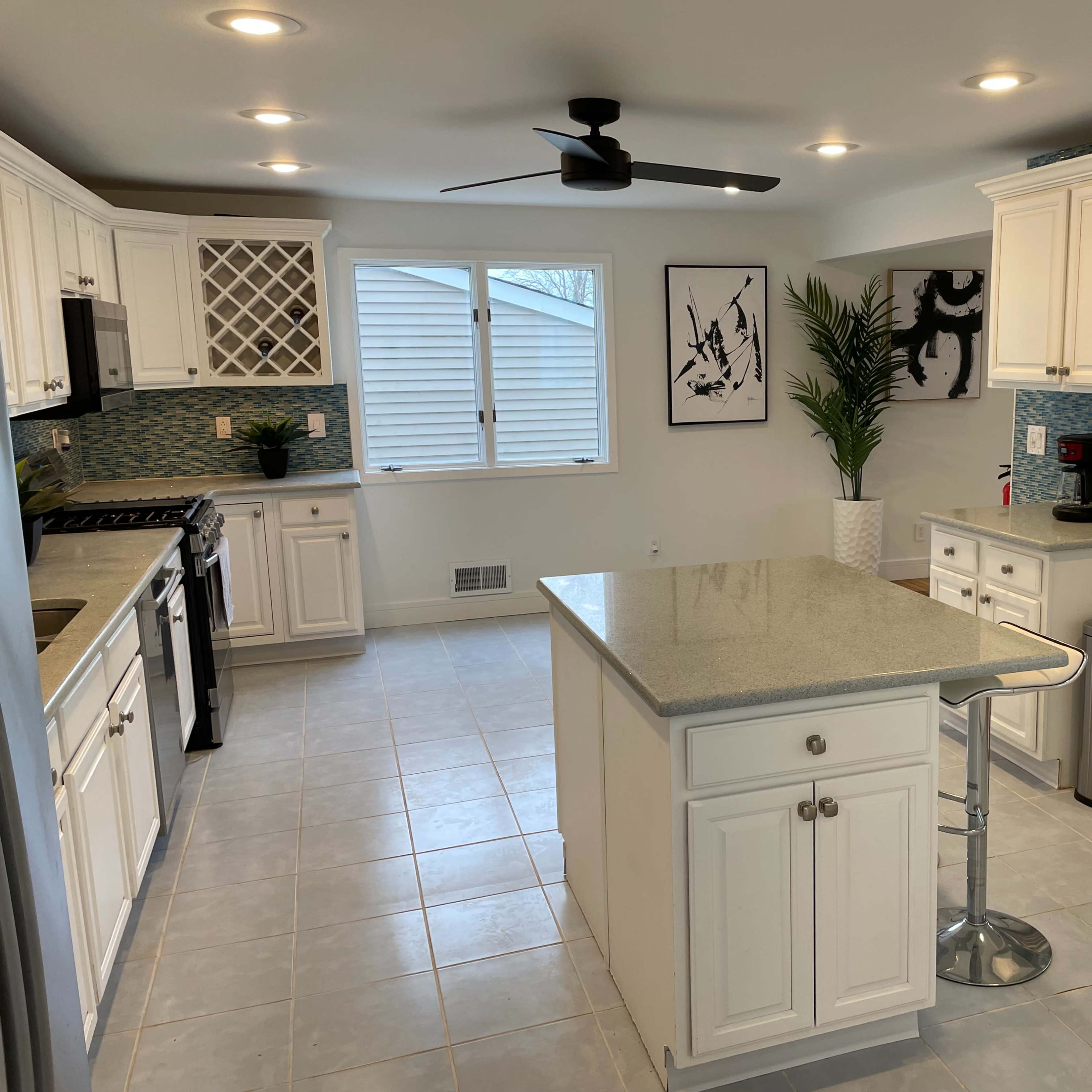 A modern kitchen with white cabinets, a central island, and a large window providing natural light.