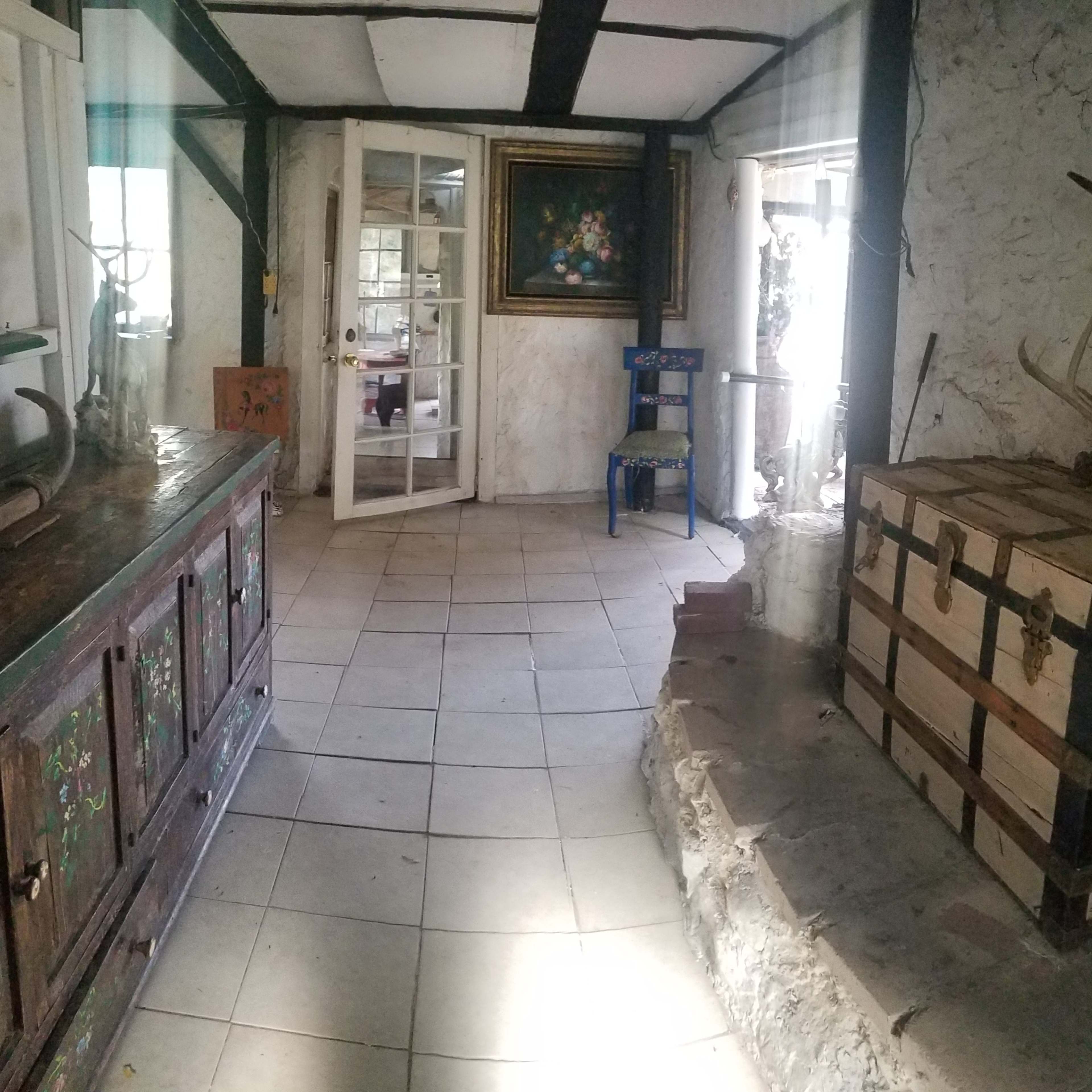 A spacious room with stone and plaster walls, featuring a wooden chest, a colorful chair, and a large painting on the wall.