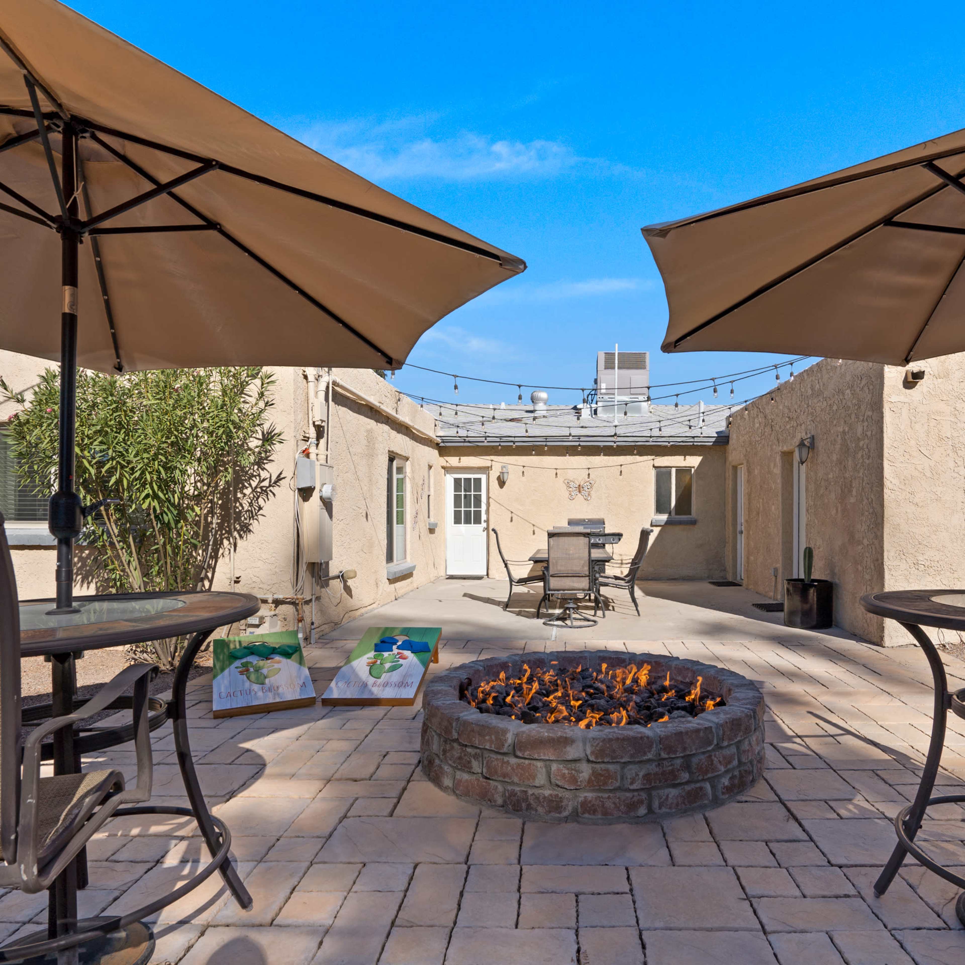 A patio area featuring two large umbrellas, a fire pit surrounded by stone, and several outdoor tables and chairs.