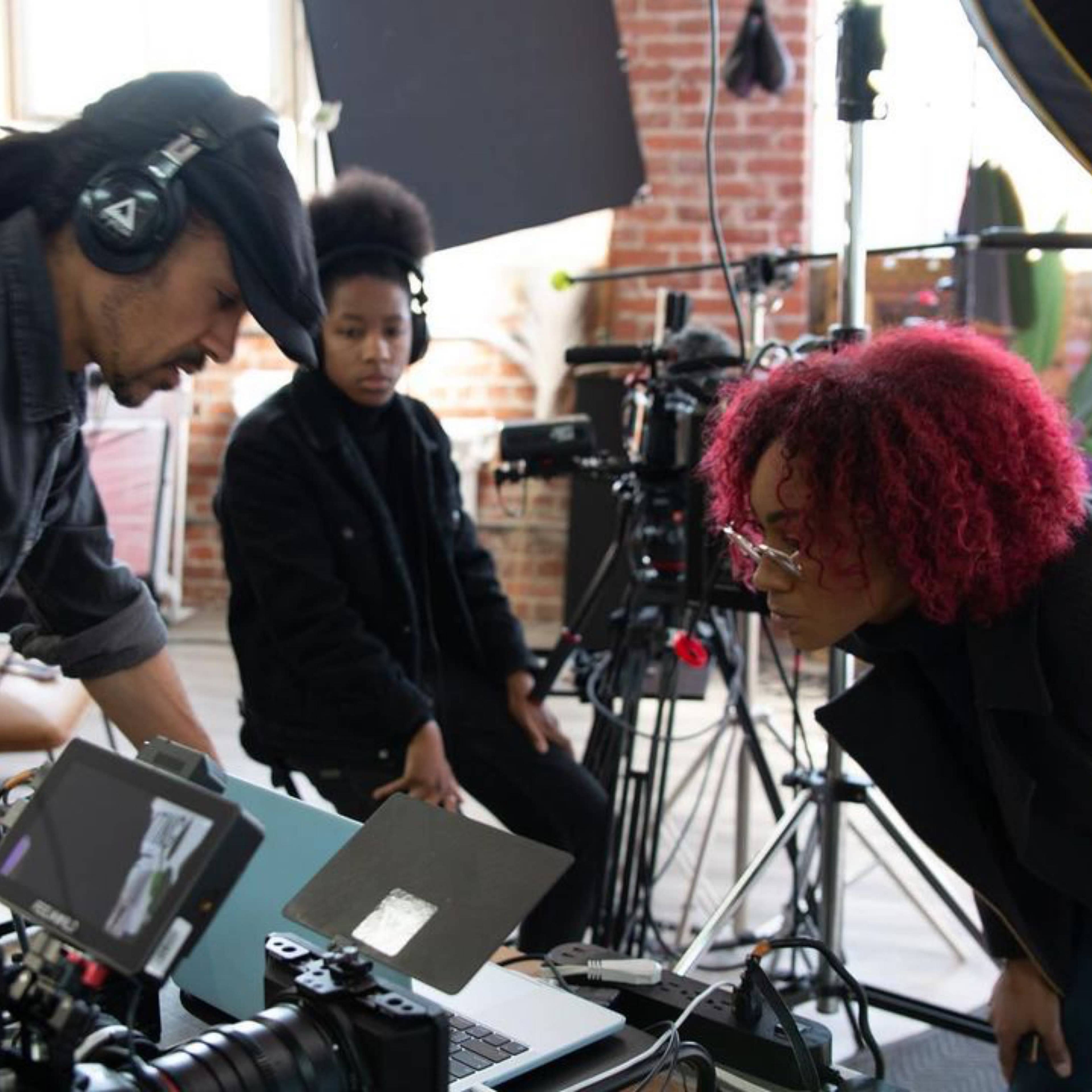 A group of filmmakers reviews footage on a laptop in a studio filled with cameras and lighting equipment.