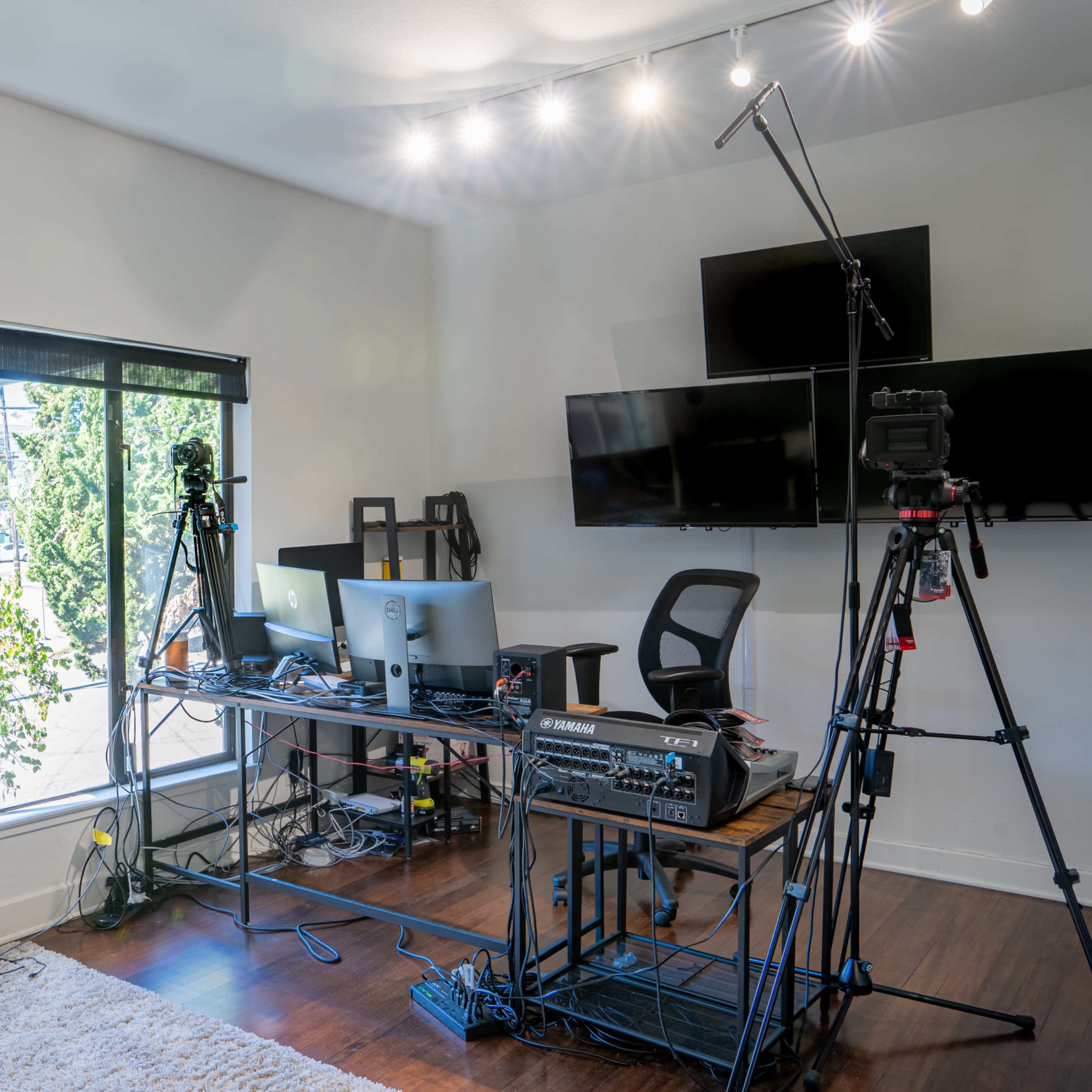 A modern office space featuring a desk with computers and camera equipment set up near a large window.