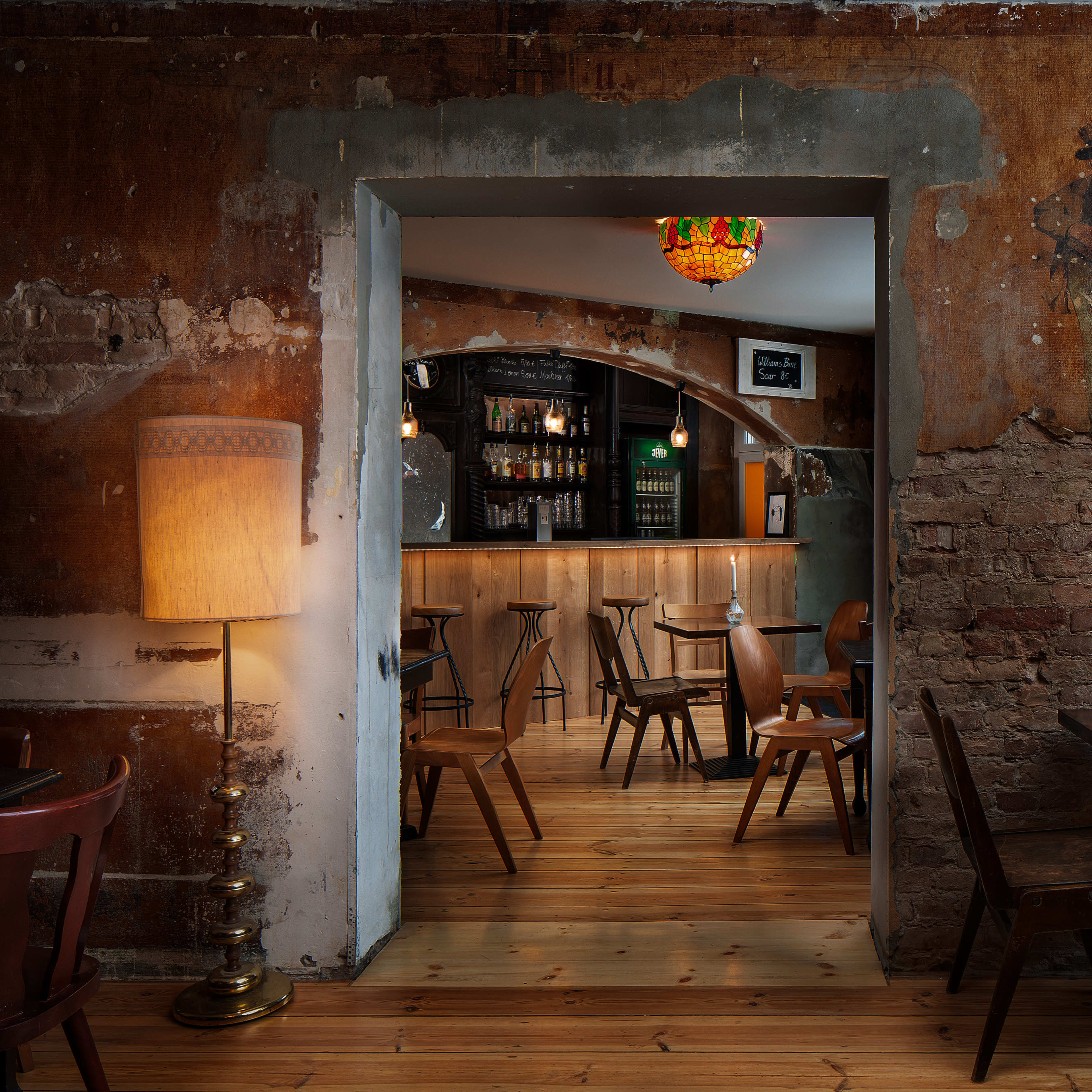 A dimly lit restaurant features rustic decor with exposed brick walls, wooden floors, and a bar area visible through an archway.