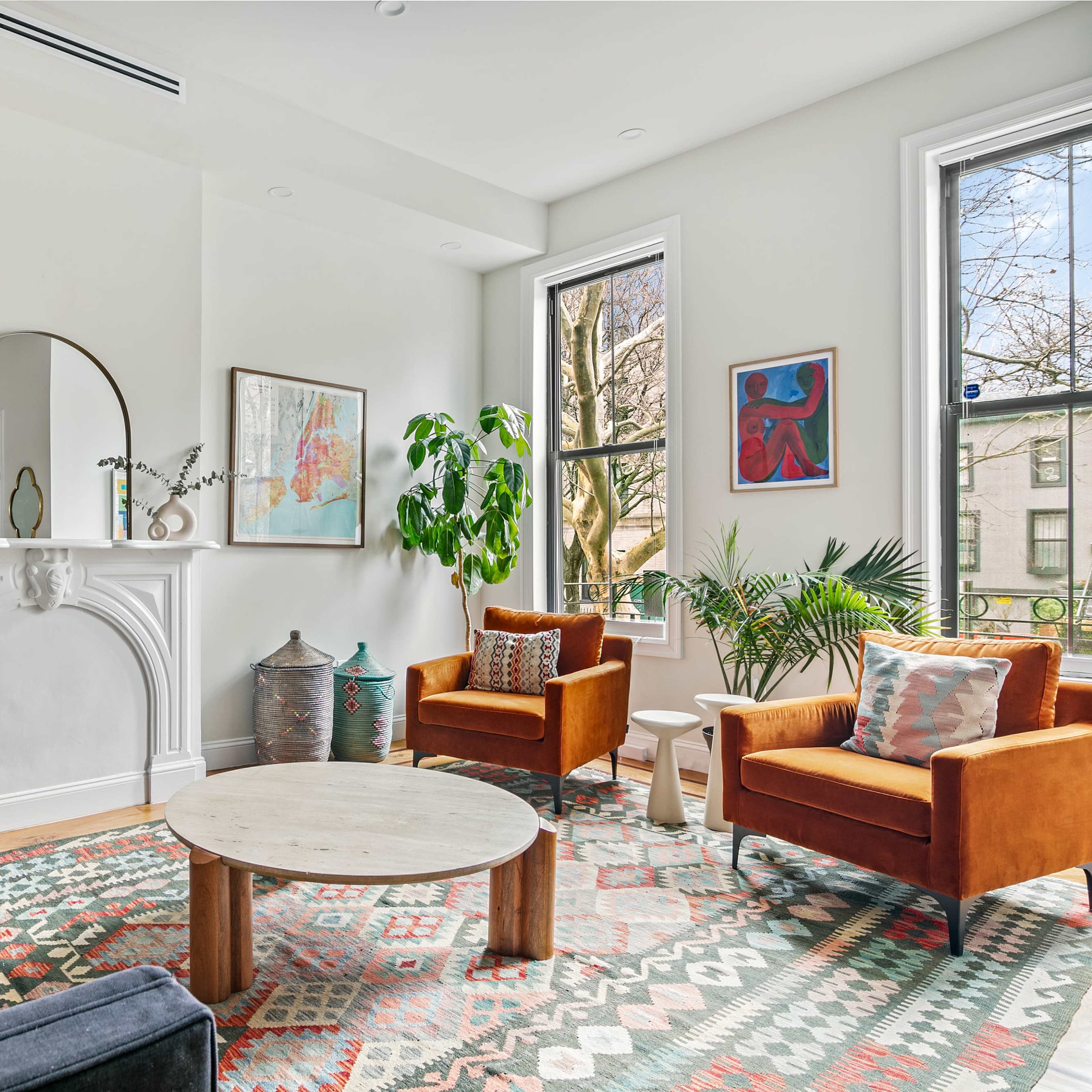 A stylish living room with a blue sofa, two brown chairs, a round wooden coffee table, and large windows letting in natural light.